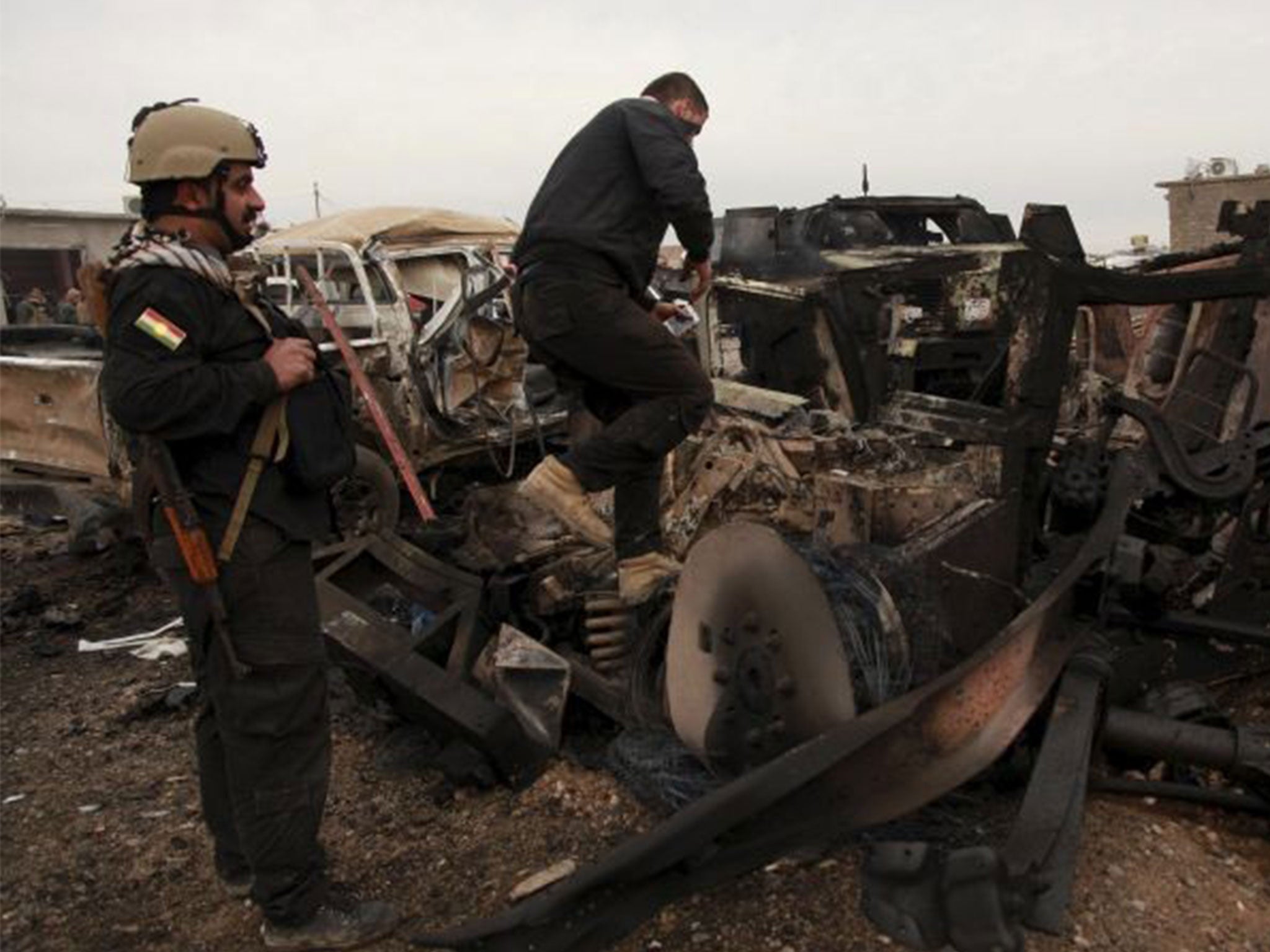 Kurdish Peshmerga fighters stand near burning vehicles during a suicide attack carried out by the Islamic State group in Kesarej village, south of Zumar, Nineveh province on 18 December 2014. Kurdish peshmerga fighters have fought their way to Iraq's Sinj