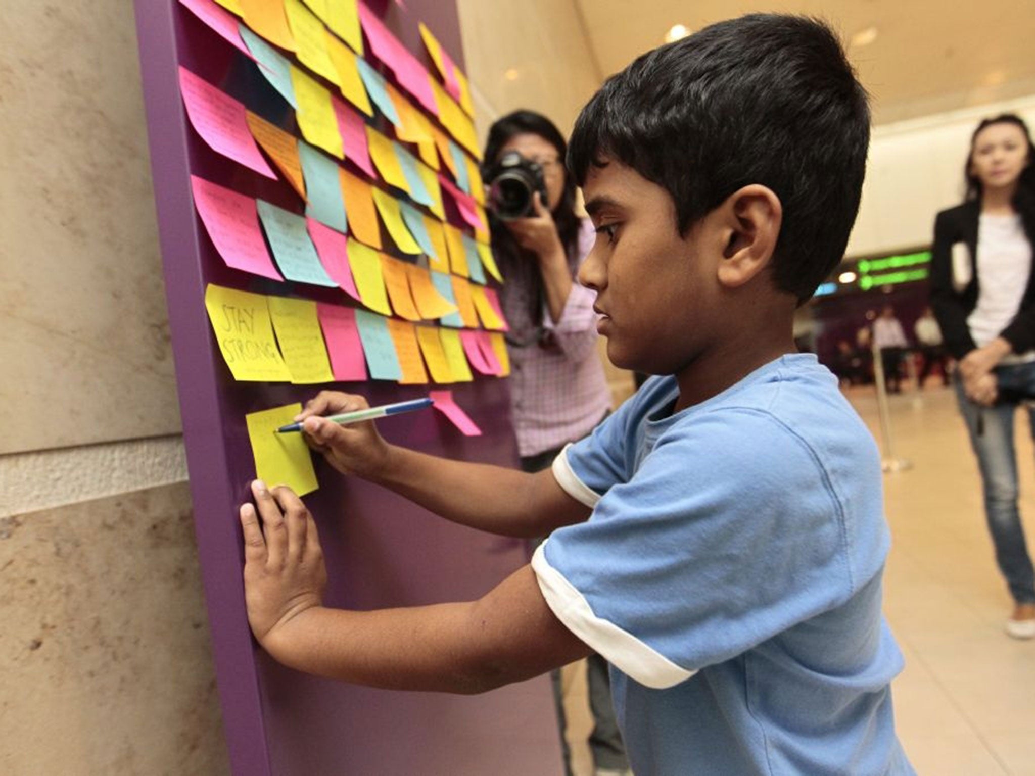 A child writes a post-it note on a board of well wishes for the passengers at Changi airport in Singapore