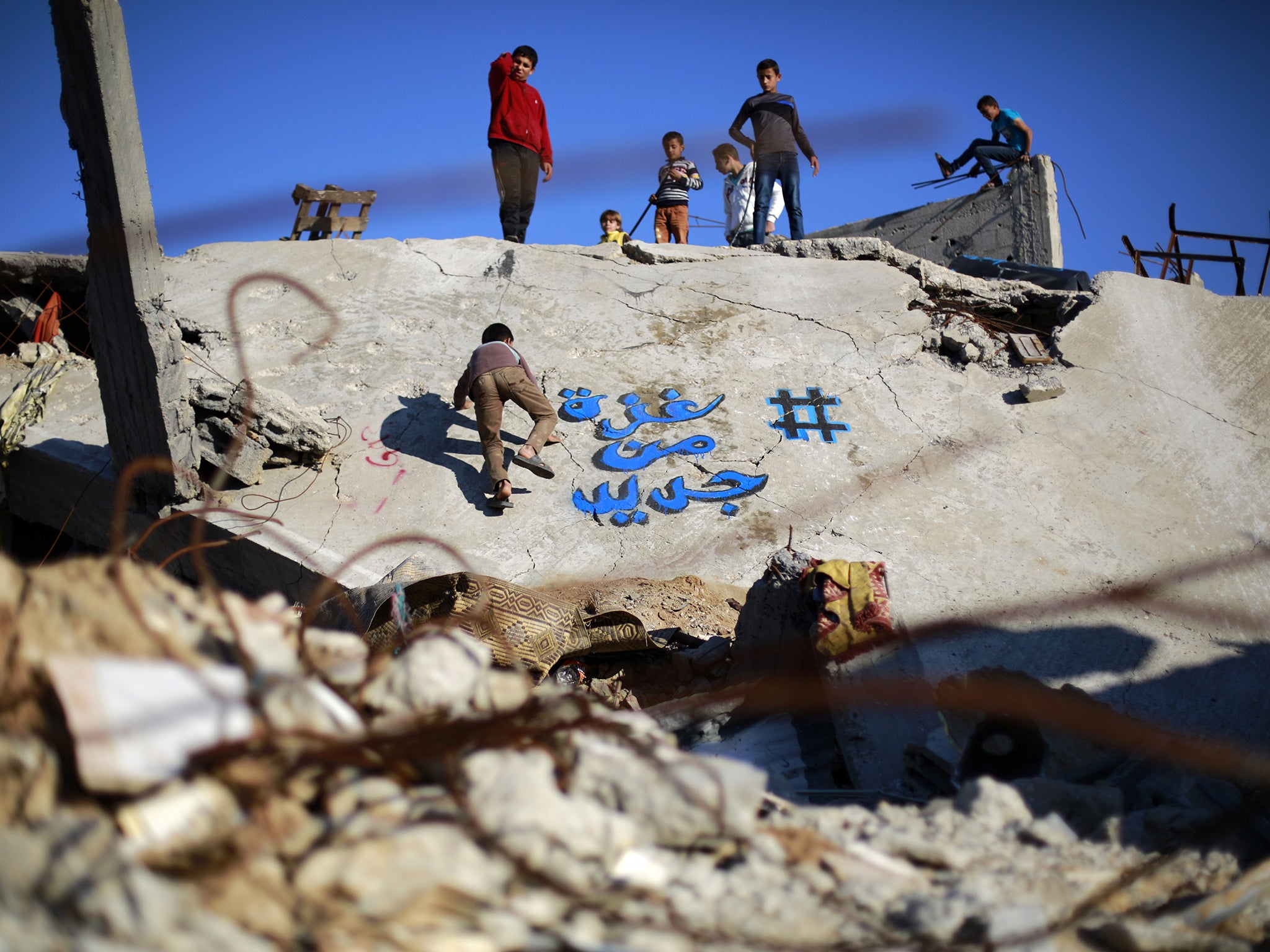 Palestinian children play on the rubble of destroyed building bearing graffiti in Gaza City's Al-Shejaiya suburb in December, 2014.