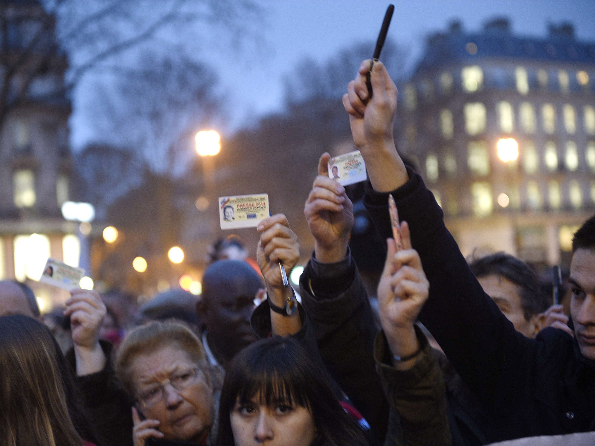 Journalists raise their press cards as others hold up pens during a vigil at the Place de la Republique