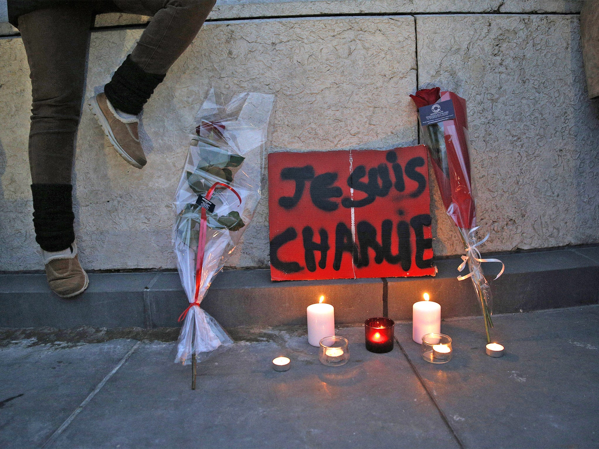 Flowers, candles and a sign reading 'I am Charlie' are placed against a wall during a demonstration in Paris