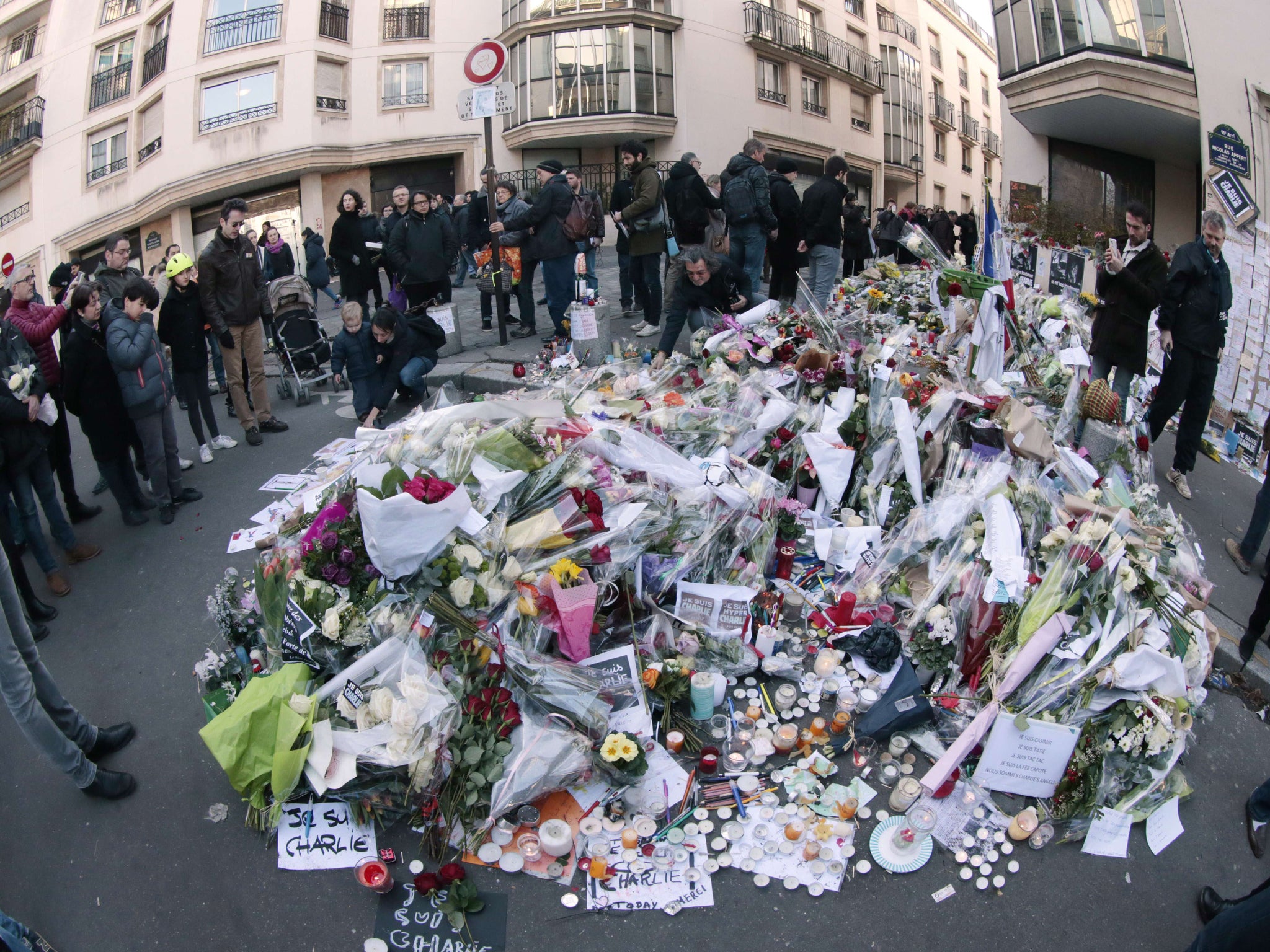 People lay flowers and candles close to the offices of the Charlie Hebdo in Paris as people gather for Sunday's march