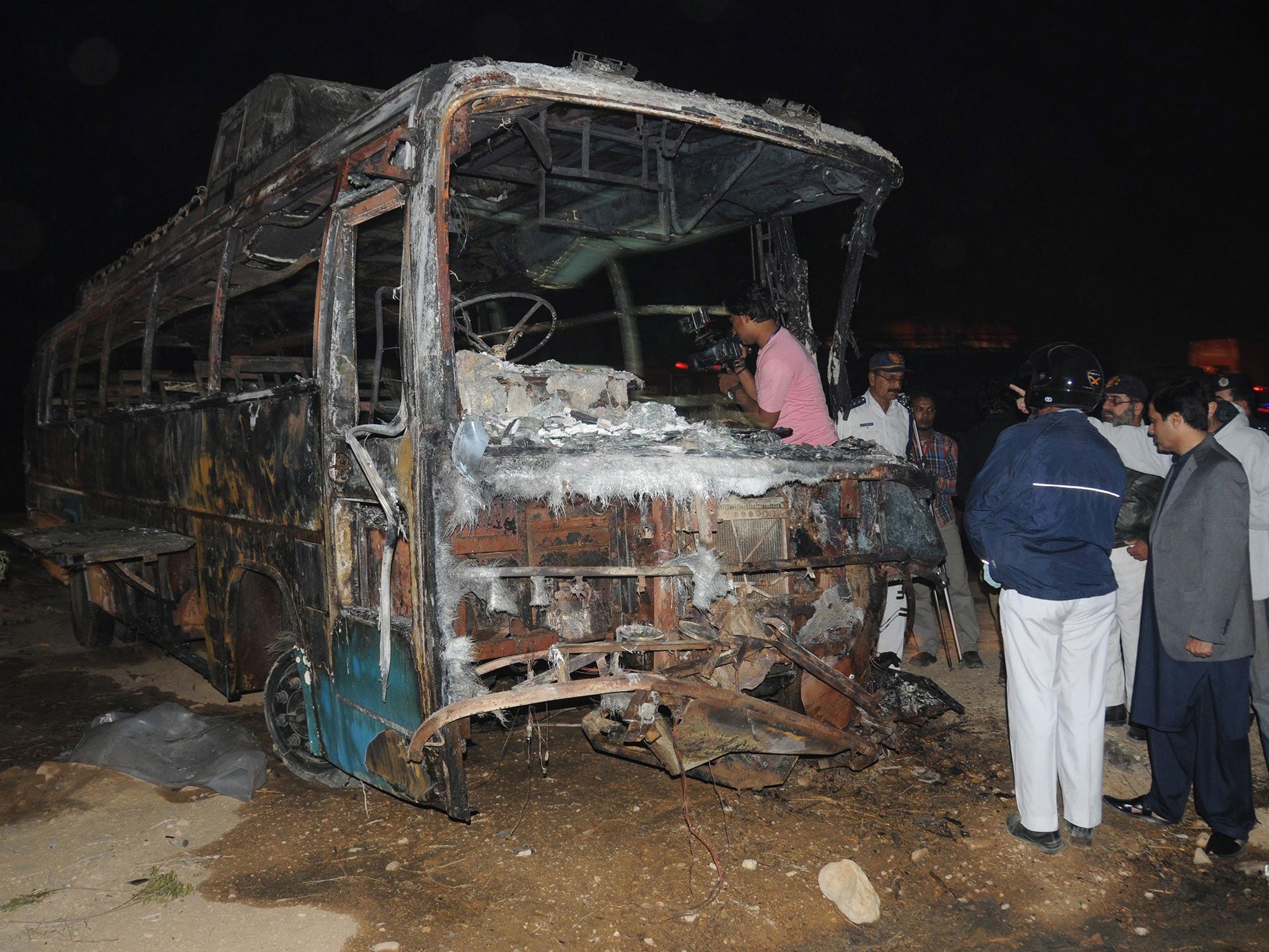 Pakistani security officials inspect the wreckage of a passenger bus after it collided with an oil tanker and burst into flames along the Super Highway near Karachi, Pakistan