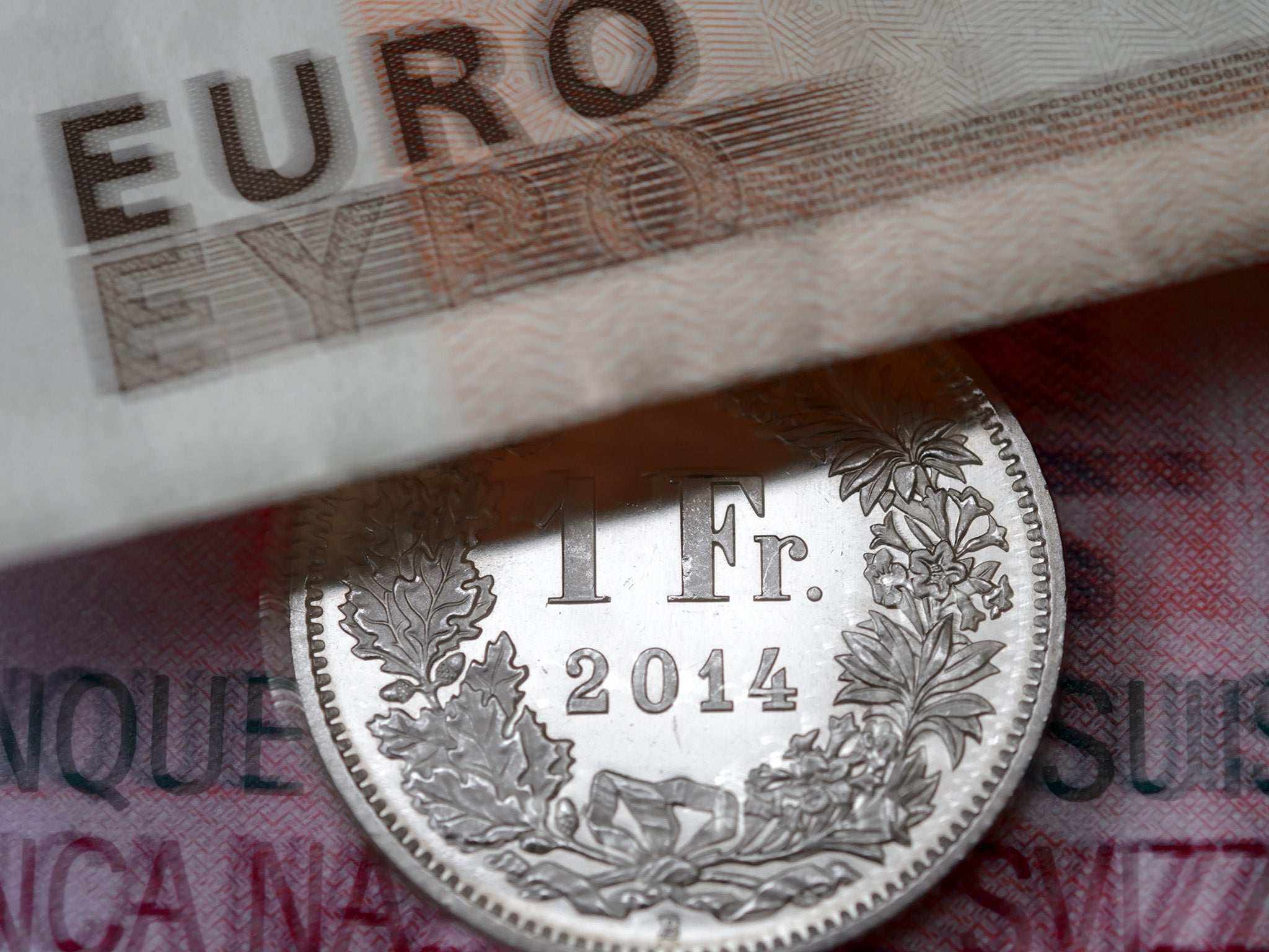 A Swiss coin is seen beneath a euro banknote.