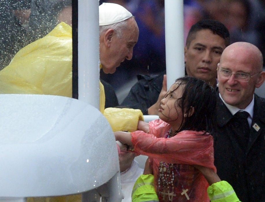 A rain-soaked girl gets held up to talk to the Pope