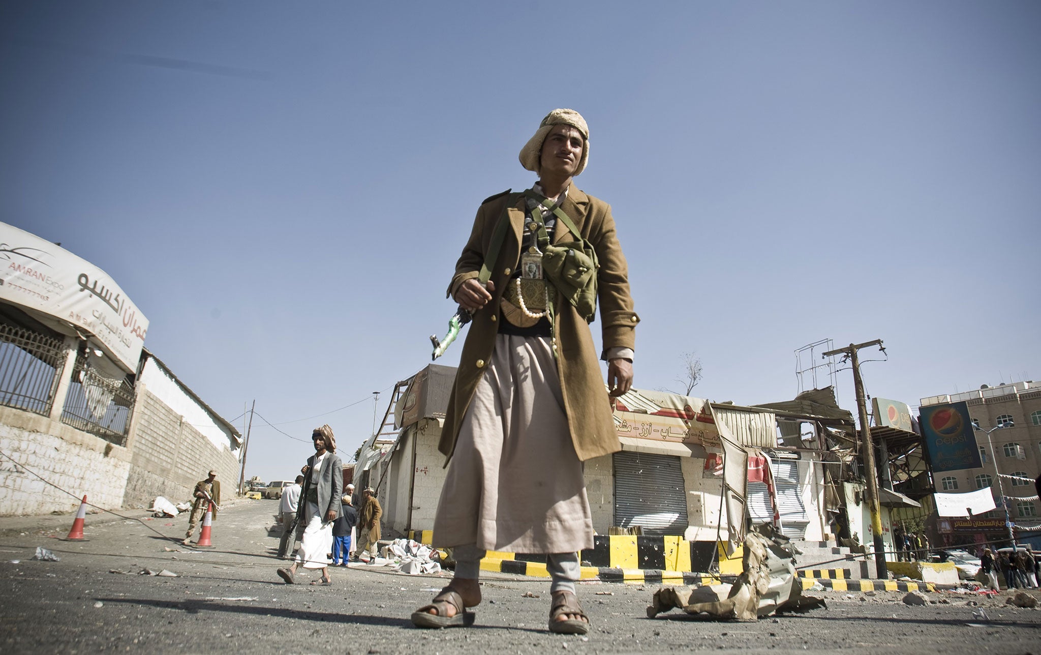 A Houthi Shiite Yemeni stands guard in front of a building damaged during recent clashes near the presidential palace in Sanaa