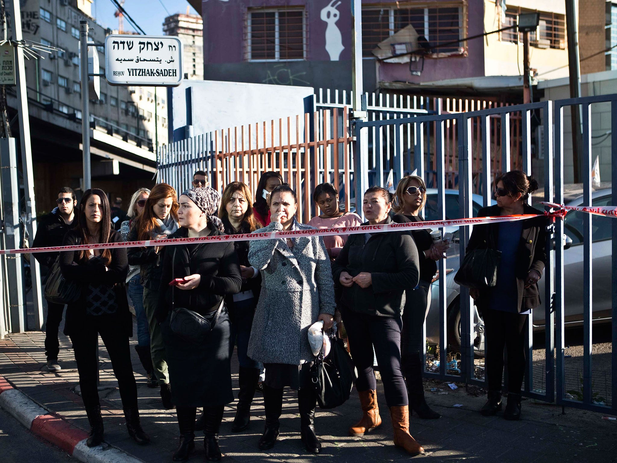 Passers-by stand behind a police tape at the scene of a stabbing attack in Tel Aviv