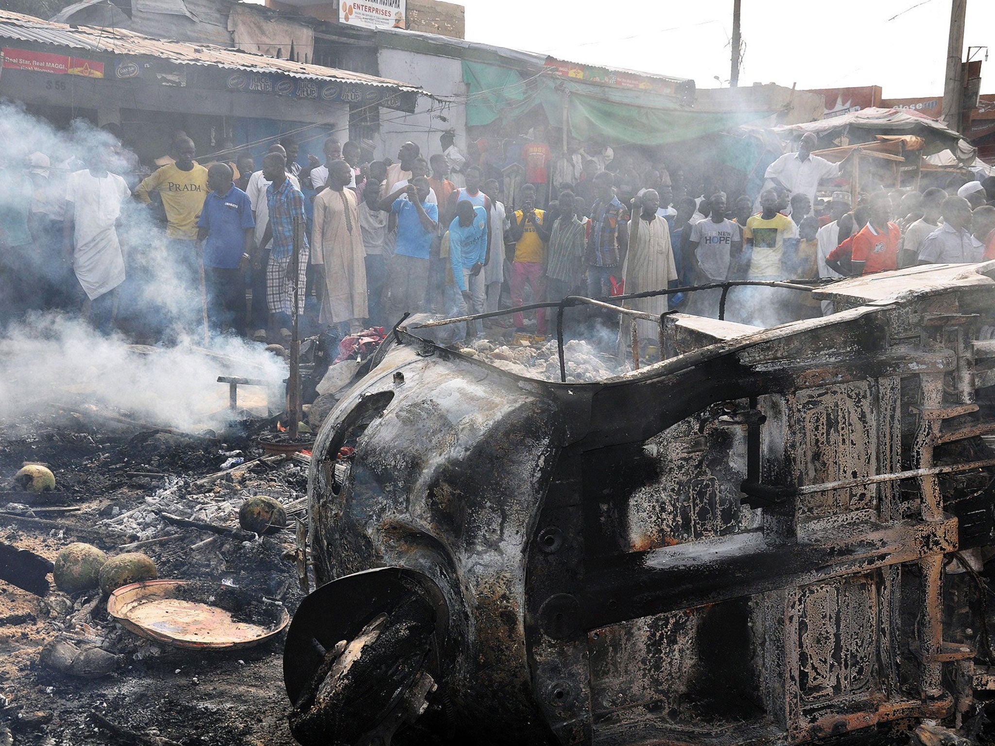 People gather to look at a burnt vehicle following a bomb explosion that rocked the busiest roundabout near the crowded Market in Maiduguri, Borno State on 1 July 2014