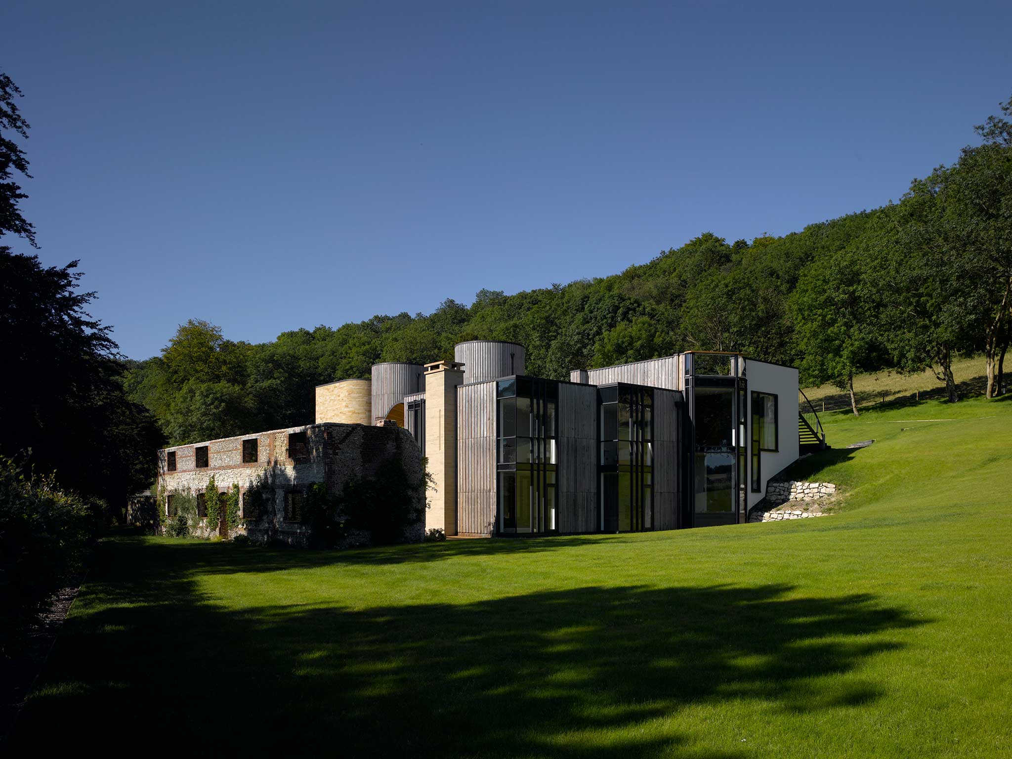 Downley House, Hants (BPR Architects): The house has a barrel-vaulted dining hall “centred on the ruin entrance”. A stair on the roof terrace “bridges into the landscape”