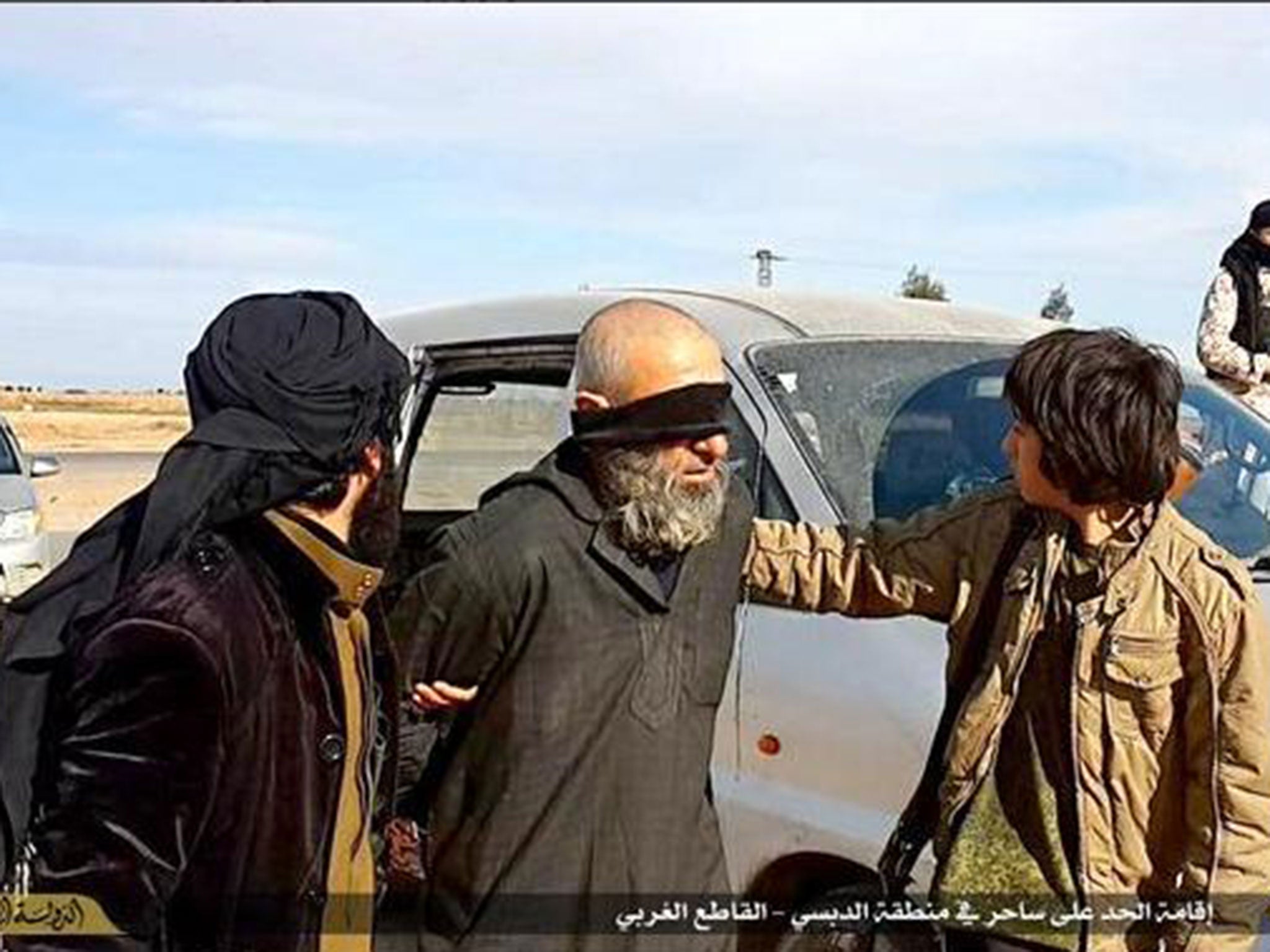 An Isis militant leads the man to a block in front of a crowd of people