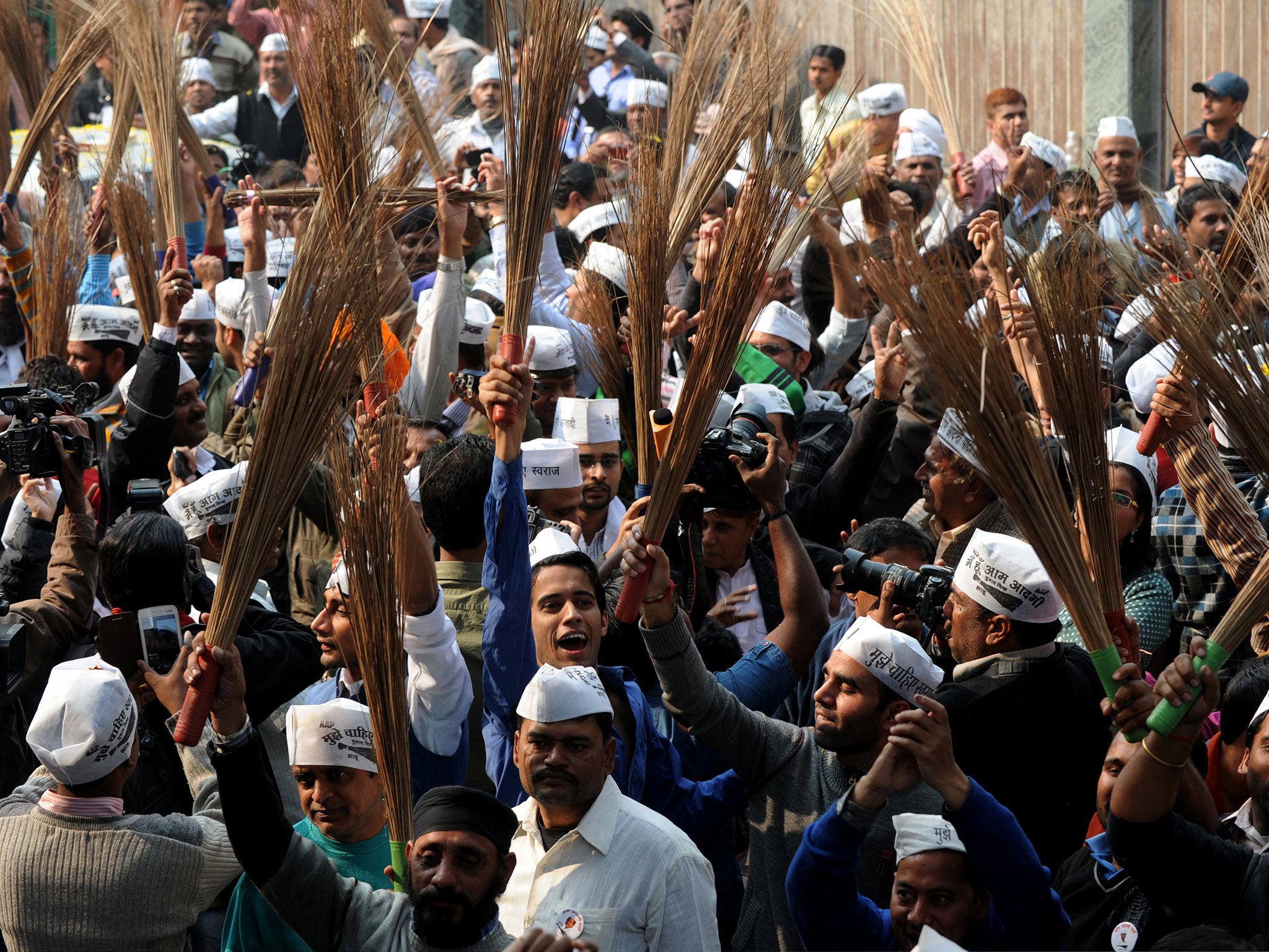 AAP supporters hold brooms, the party symbol, as they celebrate outside the party office after winning an election in 2013