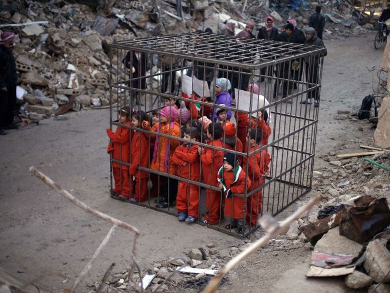 Children carry signs inside a cage during a protest against forces loyal to Syria's President Bashar al-Assad, in Douma on 15 February