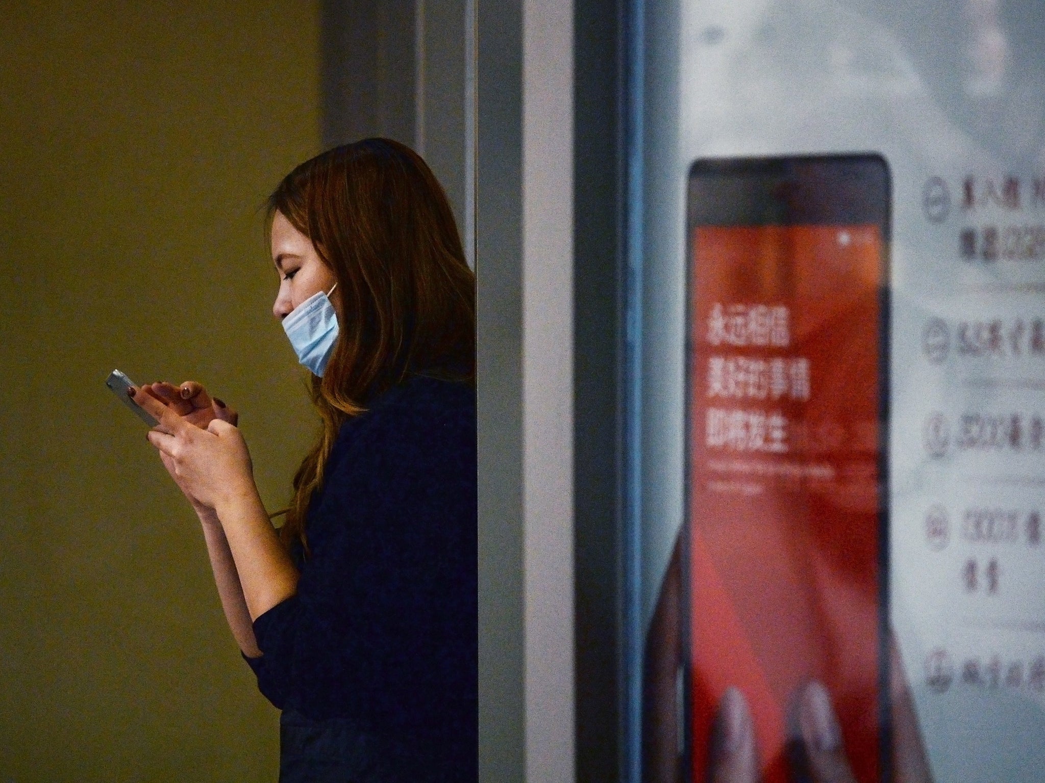 A woman wearing a mask looks at her mobile phone in a building in Beijing on January 15, 2015. Pollution levels soared in Beijing on January 15 to readings more than 20 times WHO recommended limits, as an annual bout of intense smog returned to haunt the Chinese capital despite government vows to address the plague