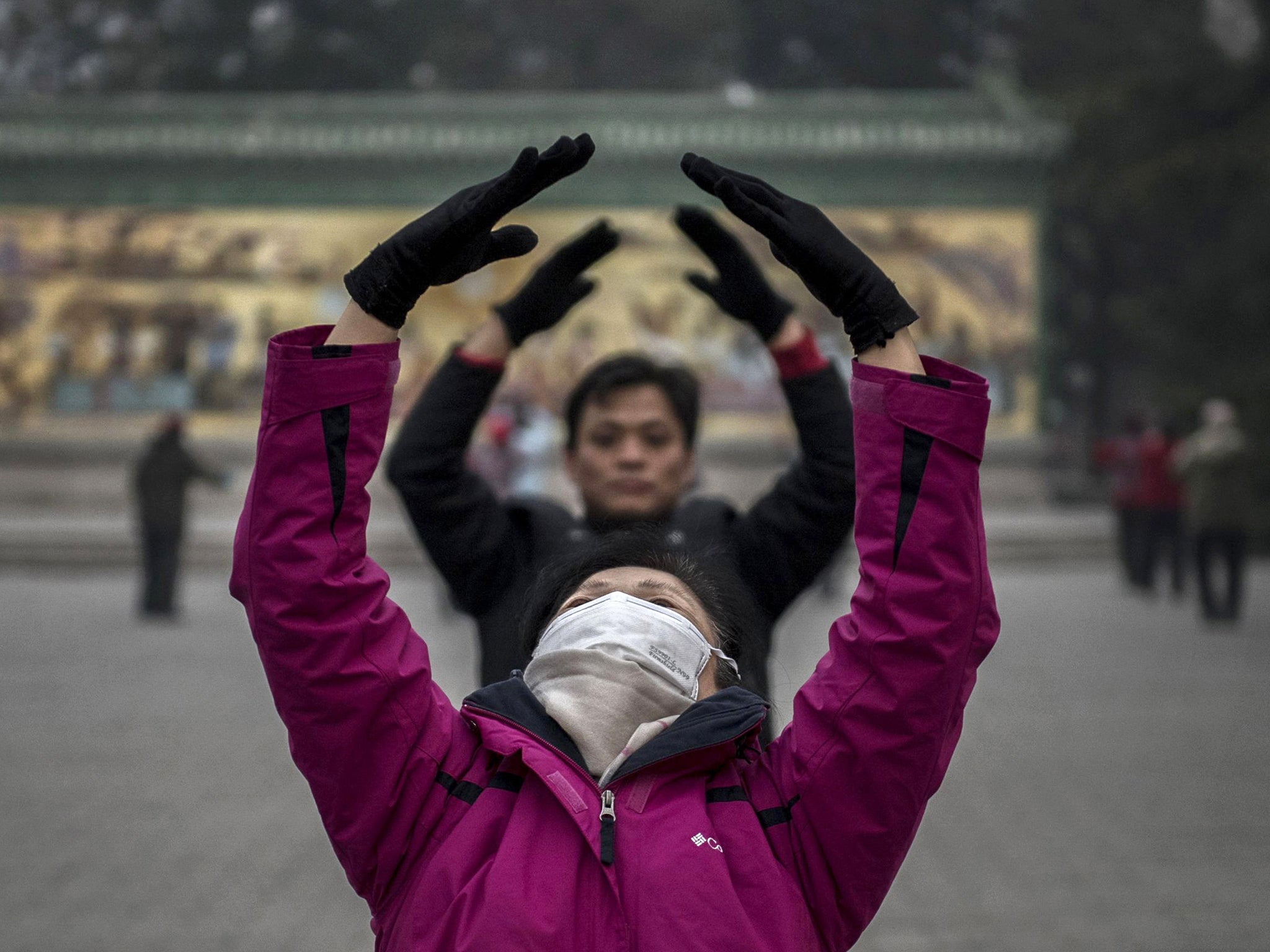 A Chinese woman wears a mask to protect herself from pollution as she and others perform Tai Chi during morning exercise