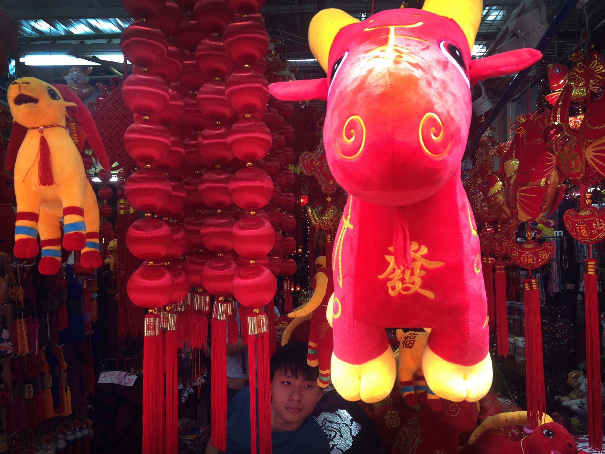 A store vender waits among Chinese New Year decorations comprising of lanterns, toy sheep and other trinkets for sale, in Singapore