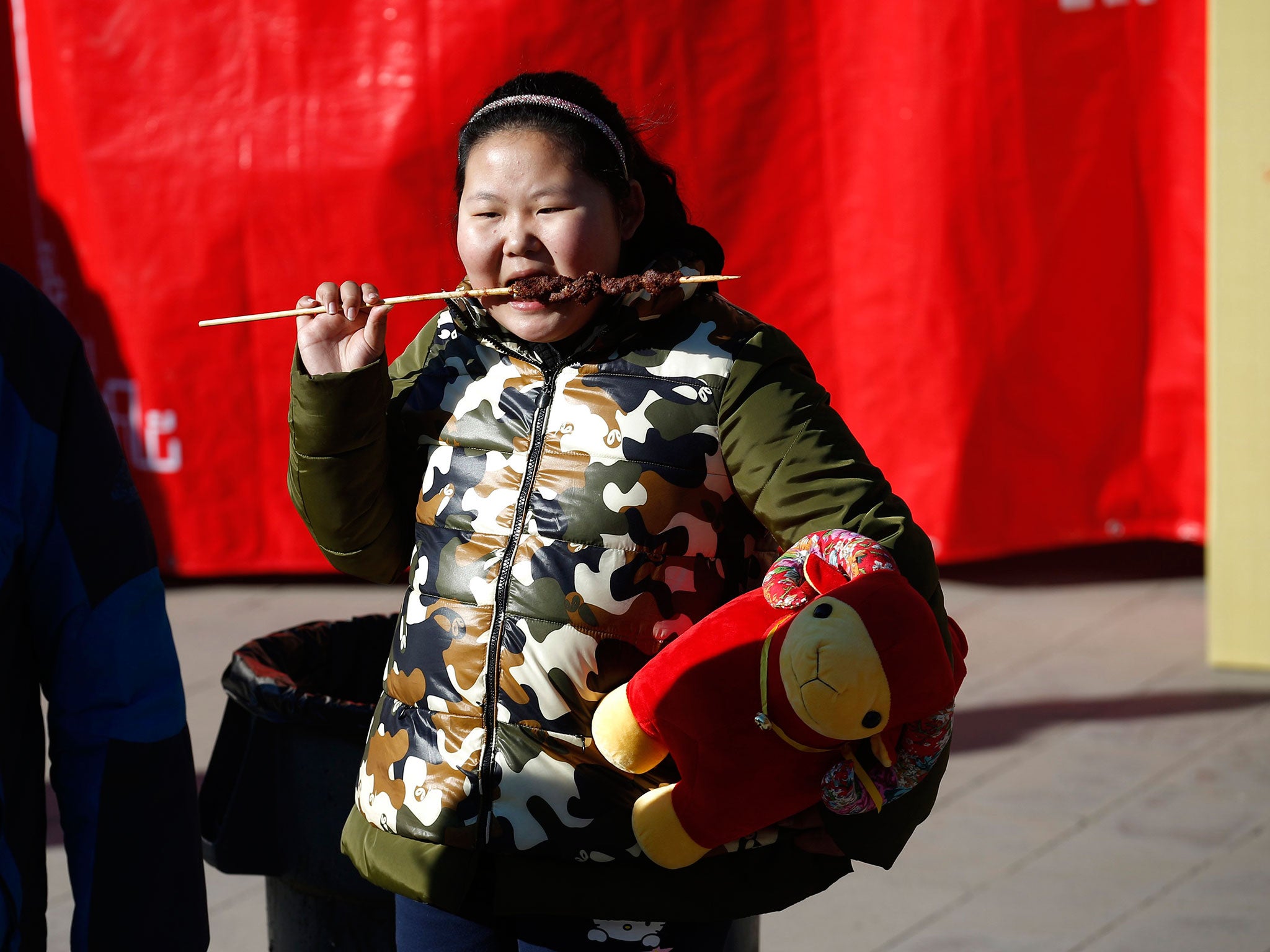 A girl, holding a sheep toy, eats at the Temple Fair, which is part of Chinese New Year celebrations at Ditan Park, in Beijing