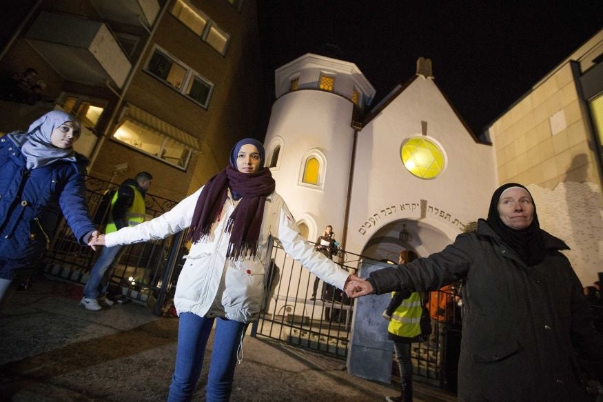 Muslim women join hands to form a human shield as they stand outside a synagogue in Oslo