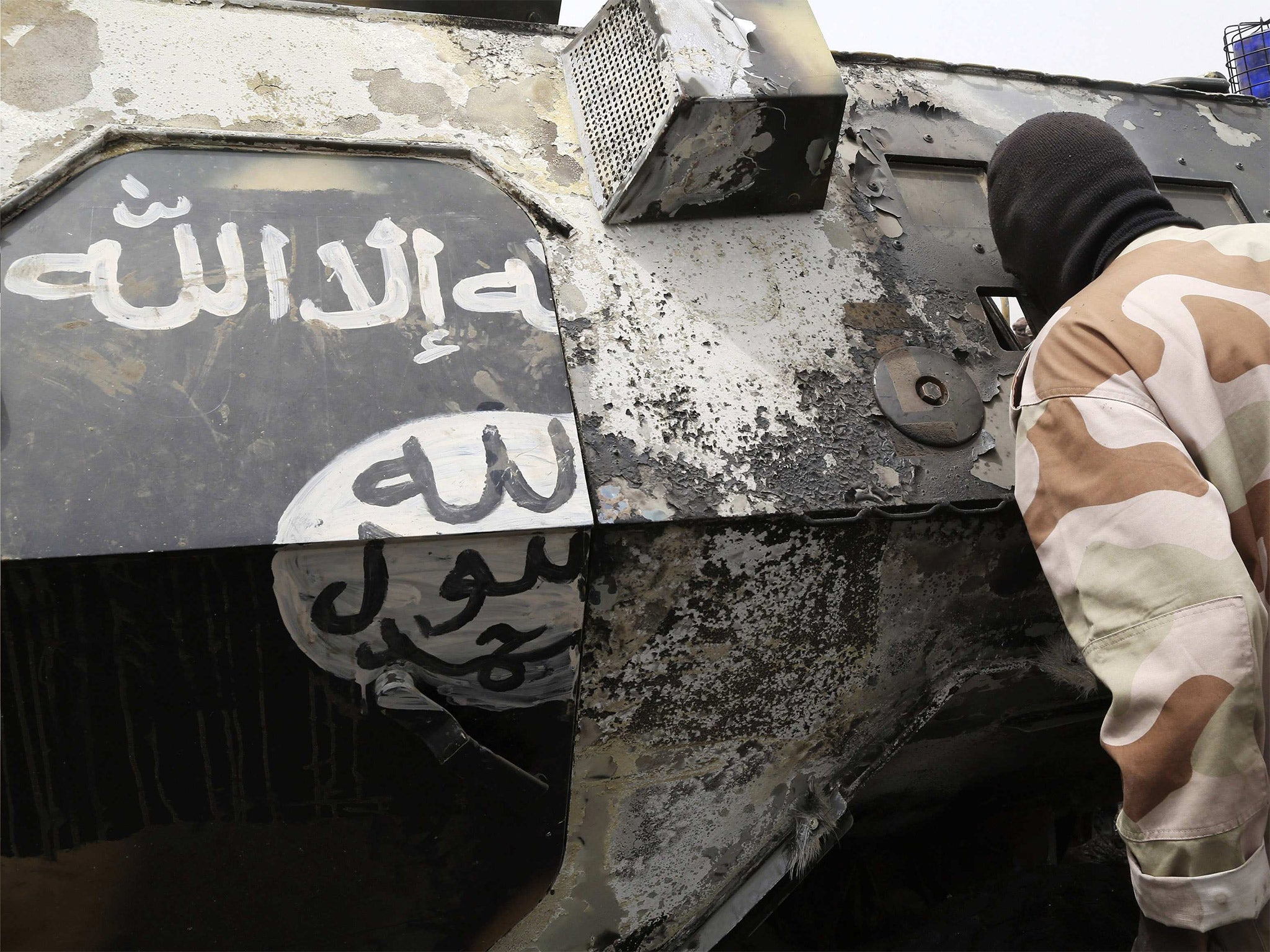 A Chadian soldier peers into a burnt armoured vehicle displaying the black and white markings of insurgent group Boko Haram