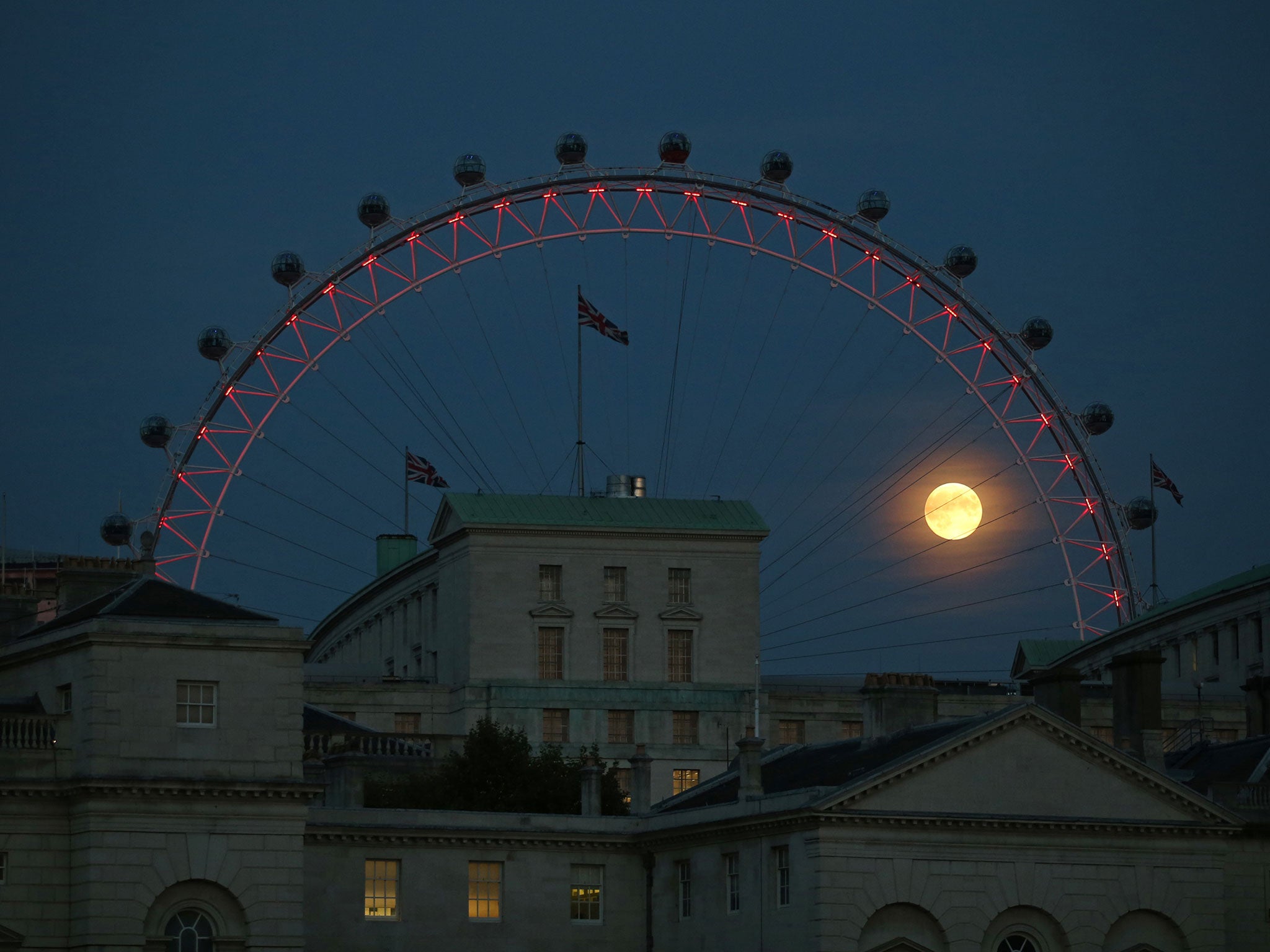 The near full moon is glimpsed through The London Eye ferris wheel view over Whitehall in September 2014