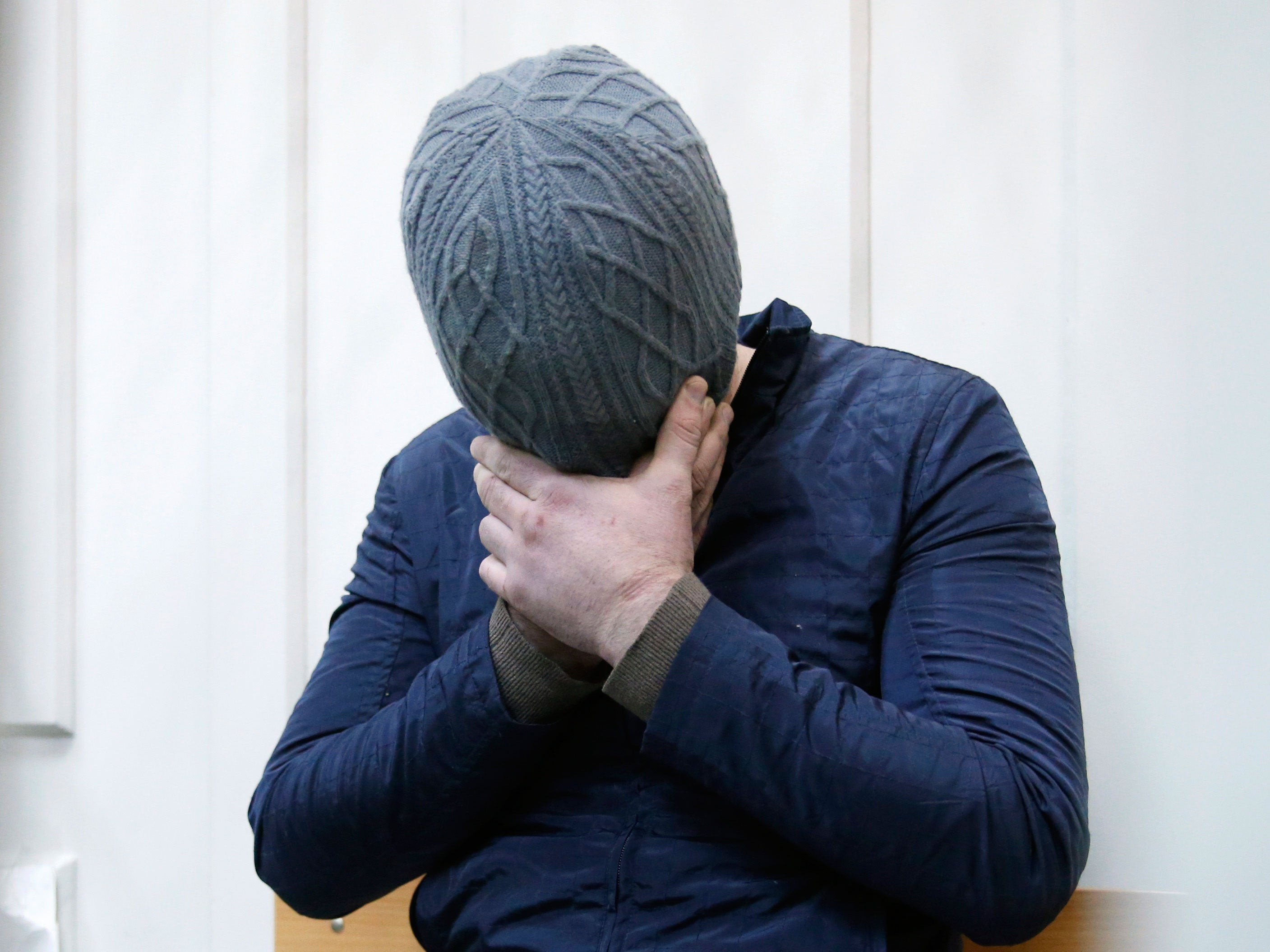 Anzor Gubashev hides his face as he sits inside a defendants' cage