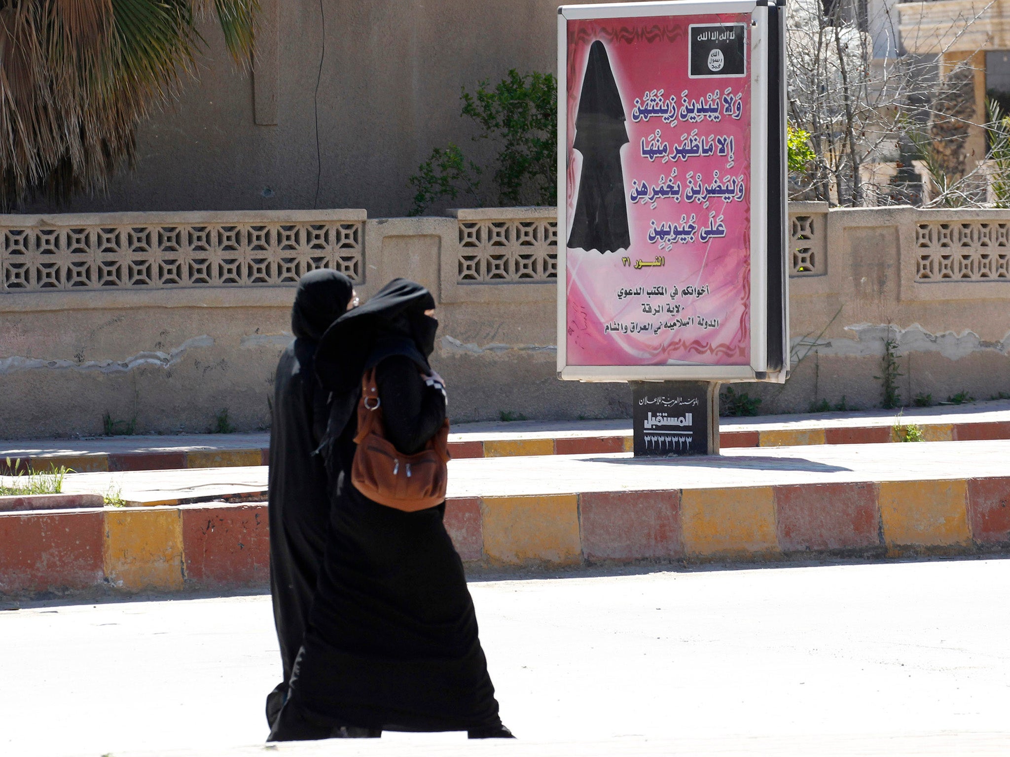 Veiled women walk past a billboard that carries a verse from Koran urging women to wear a hijab in the northern province of Raqqa