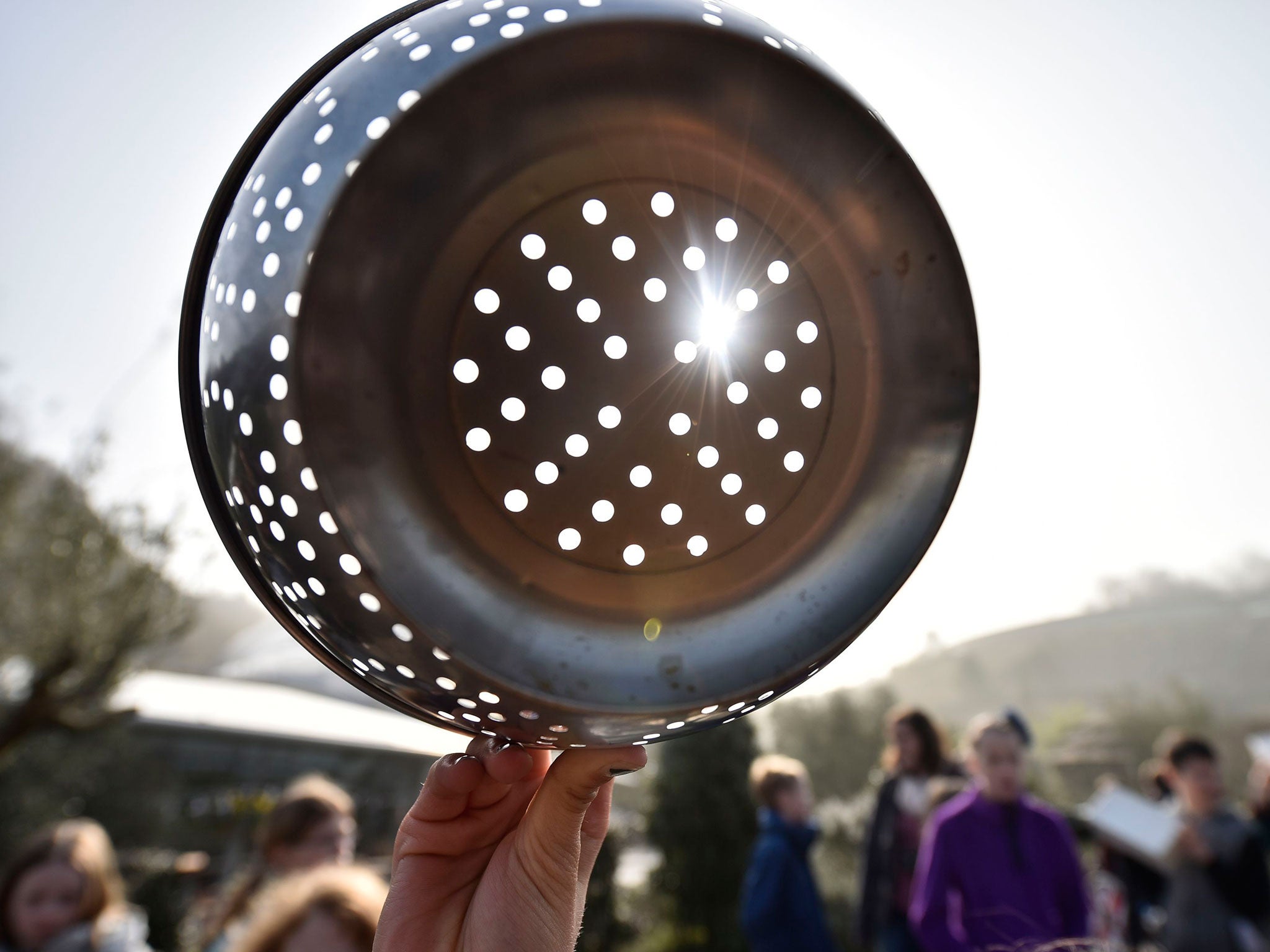 People watch the eclipse of the sun through a colander, over the Eden Project near St Austell in Cornwall