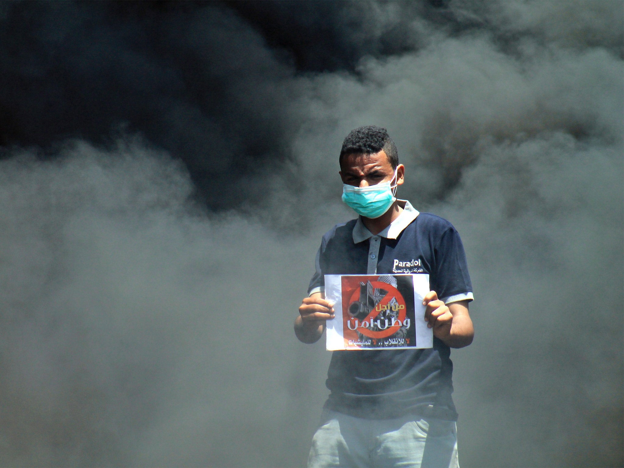 A Yemeni protester holds a placard reading 'For the sake of a secure country' in front of burning tires during an anti-Houthis protest in the central highland city of Taiz, Yemen, on Tuesday