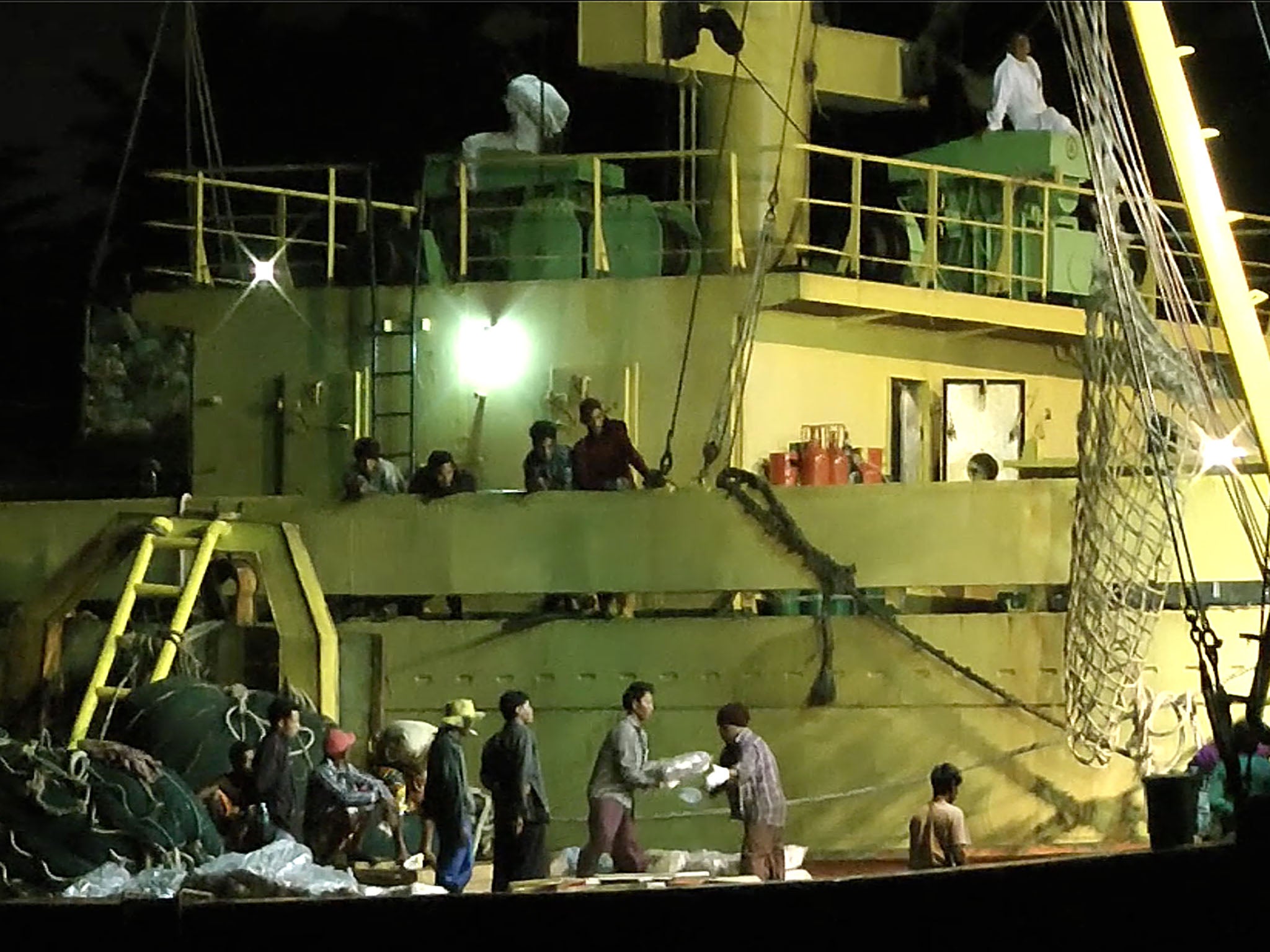 Workers from Myanmar load fish onto a Thai-flagged cargo ship in Benjina, Indonesia. An intricate web of connections separates the fish we eat from the men who catch it, and obscures a brutal truth: Your seafood may come from slaves. (AP Photo/APTN)