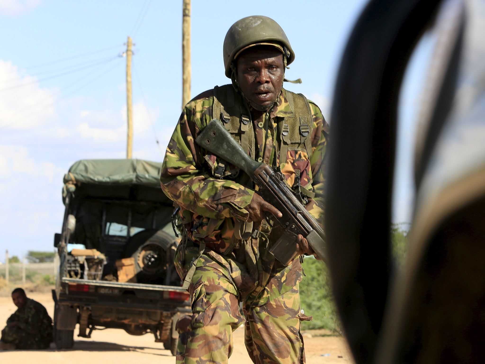 A Kenya Defense Force soldier runs for cover near the perimeter wall where attackers are holding up at a campus in Garissa