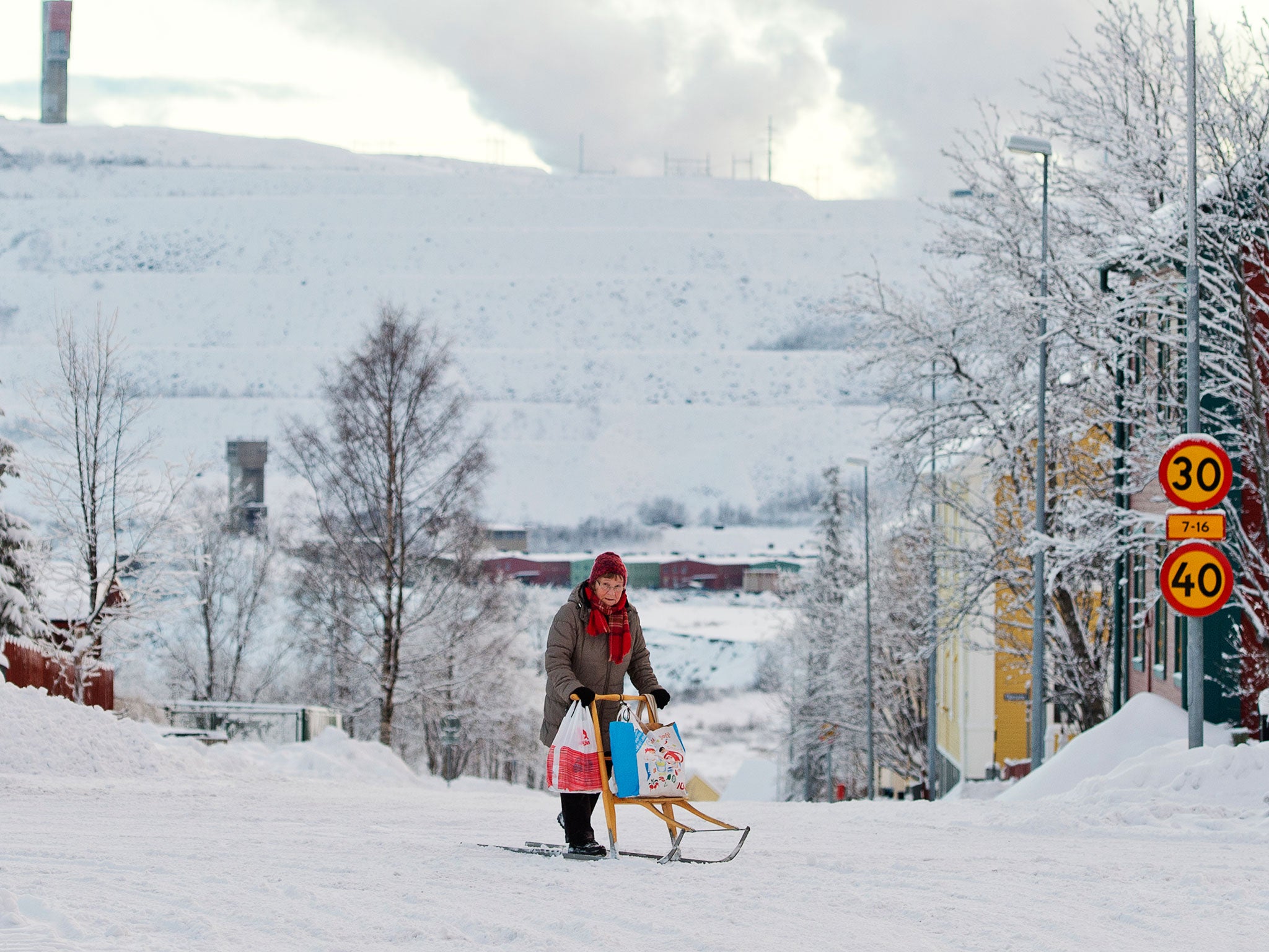 A woman rides her kick sled on a snow covered road as the iron mine of Swedish state-owned mining company LKAB (Luossavaara-Kiirunavaara Aktiebolag) at Sweden's northernmost town of Kiruna, situated in the province of Lapland is pictured on November 5, 20