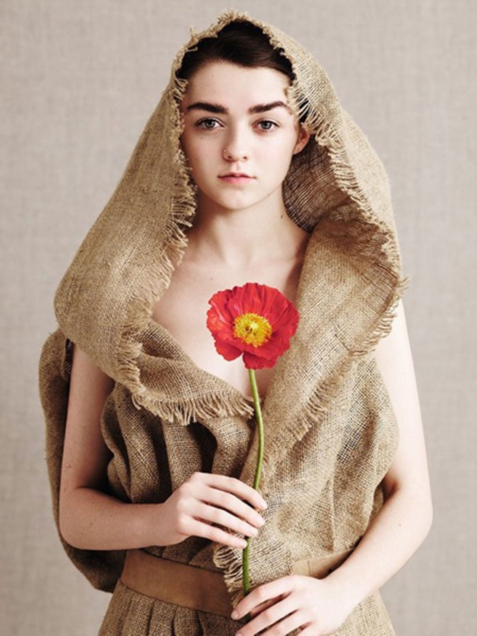 Maisie Williams (Arya Stark) holds a red flowers and sports a Gareth Pugh dress