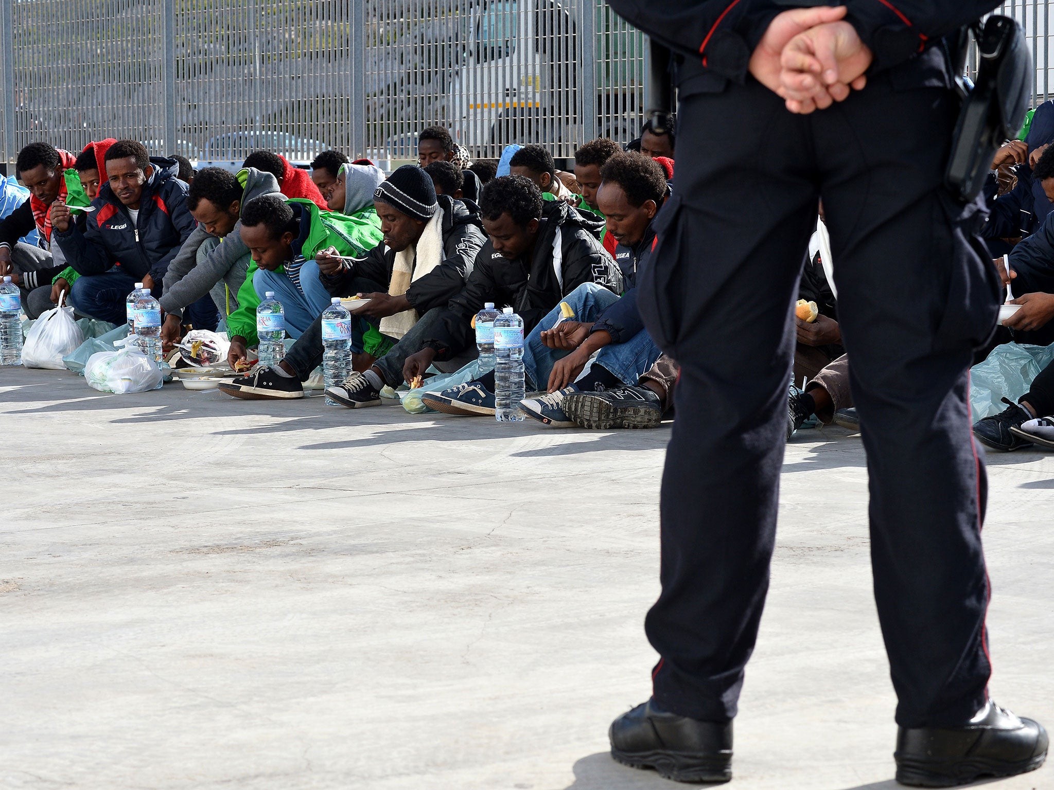 An Italian policeman stands guard as migrants eat while waiting at the port of Lampedusa to board a ferry bound for Porto Empedocle in Sicily. Authorities on the Italian island of Lampedusa struggled to cope with a huge influx of newly-arrived migrants as