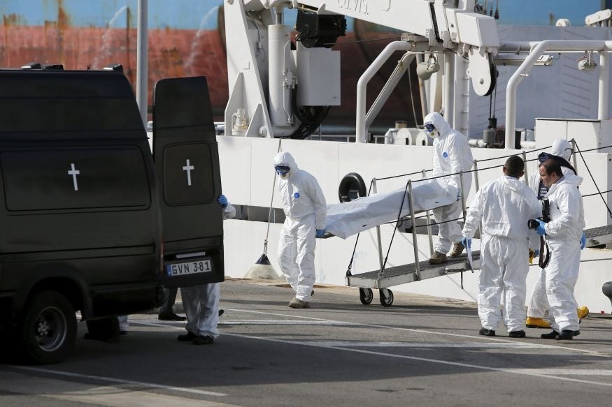 Coastguard personnel in protective clothing carry the body of a dead migrant off a ship in Senglea, Malta