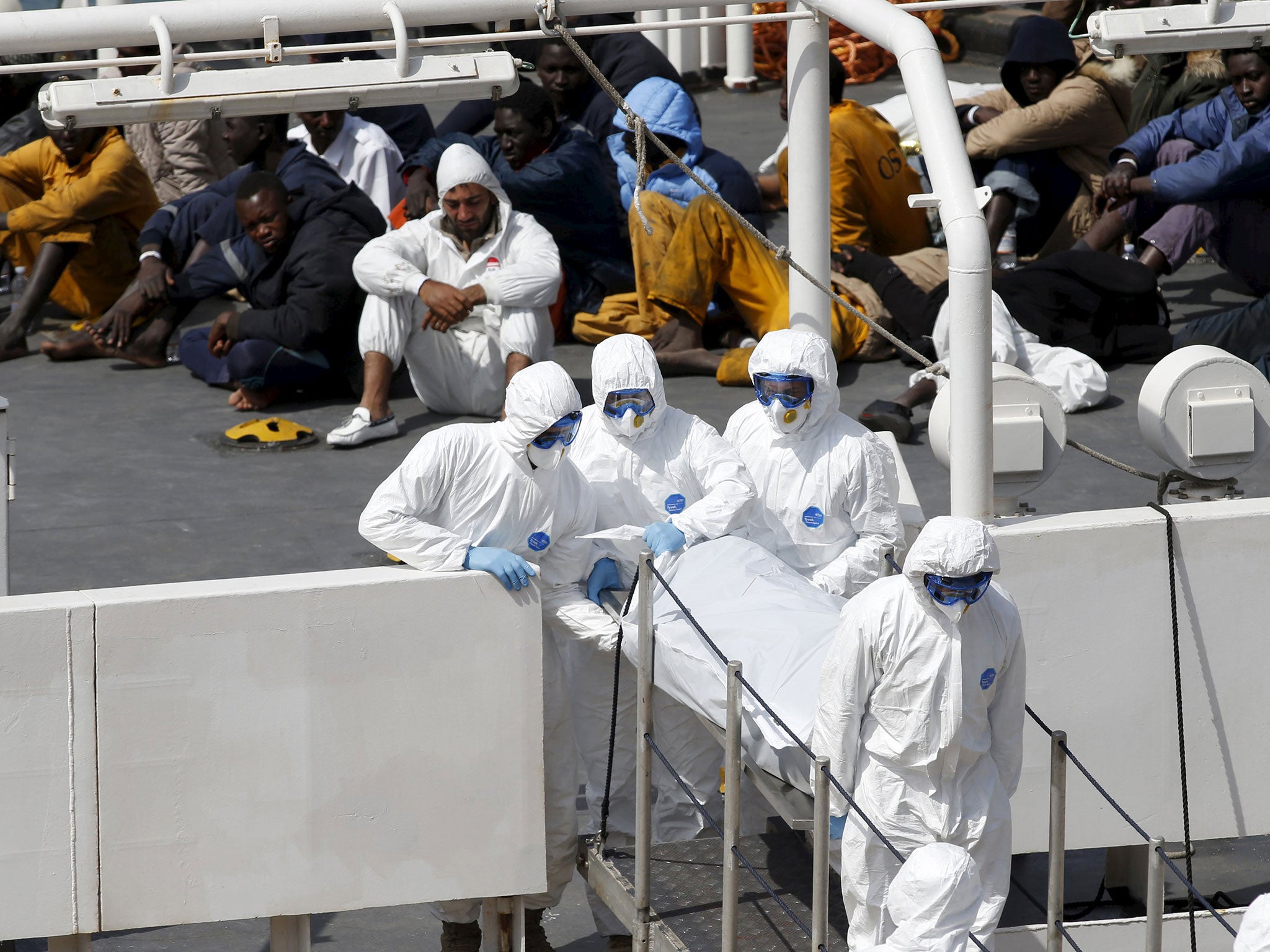 Armed Forces of Malta personnel in protective clothing carry the body of a dead immigrant off Italian coastguard ship