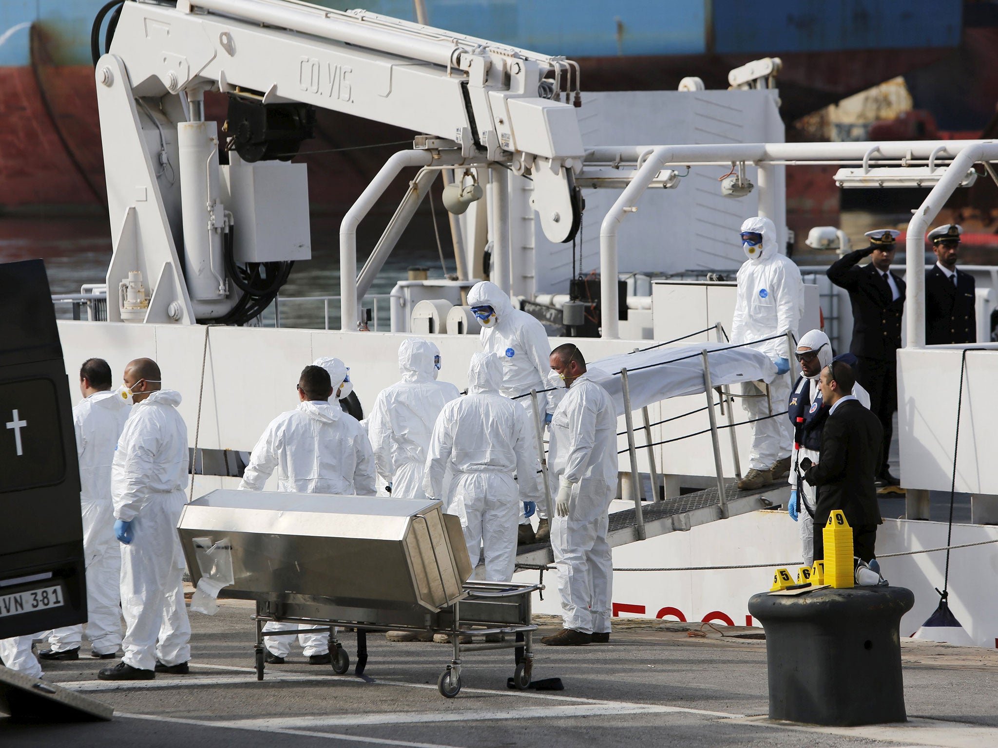 Italian coastguard personnel in protective clothing carry the body of a dead immigrant off their ship Bruno Gregoretti in Senglea