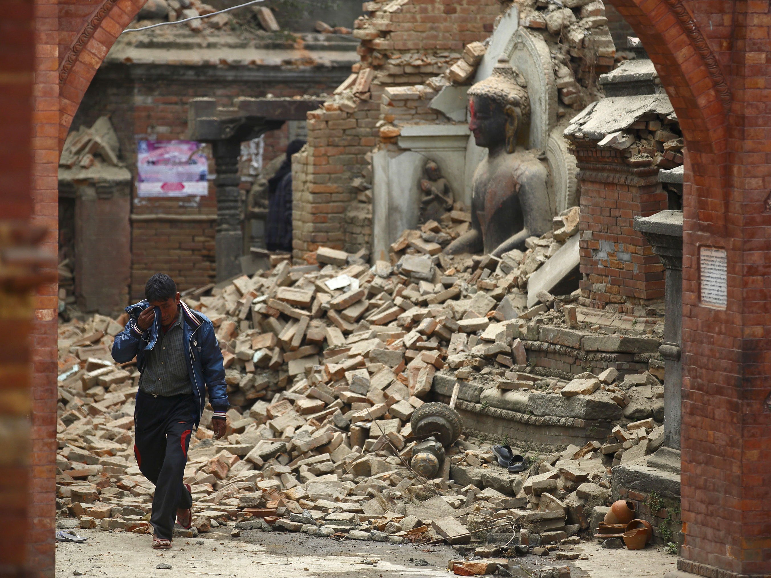 A man cries as he walks on the street while passing through a damaged statue of Lord Buddha a day after the earthquake in Bhaktapur, Nepal