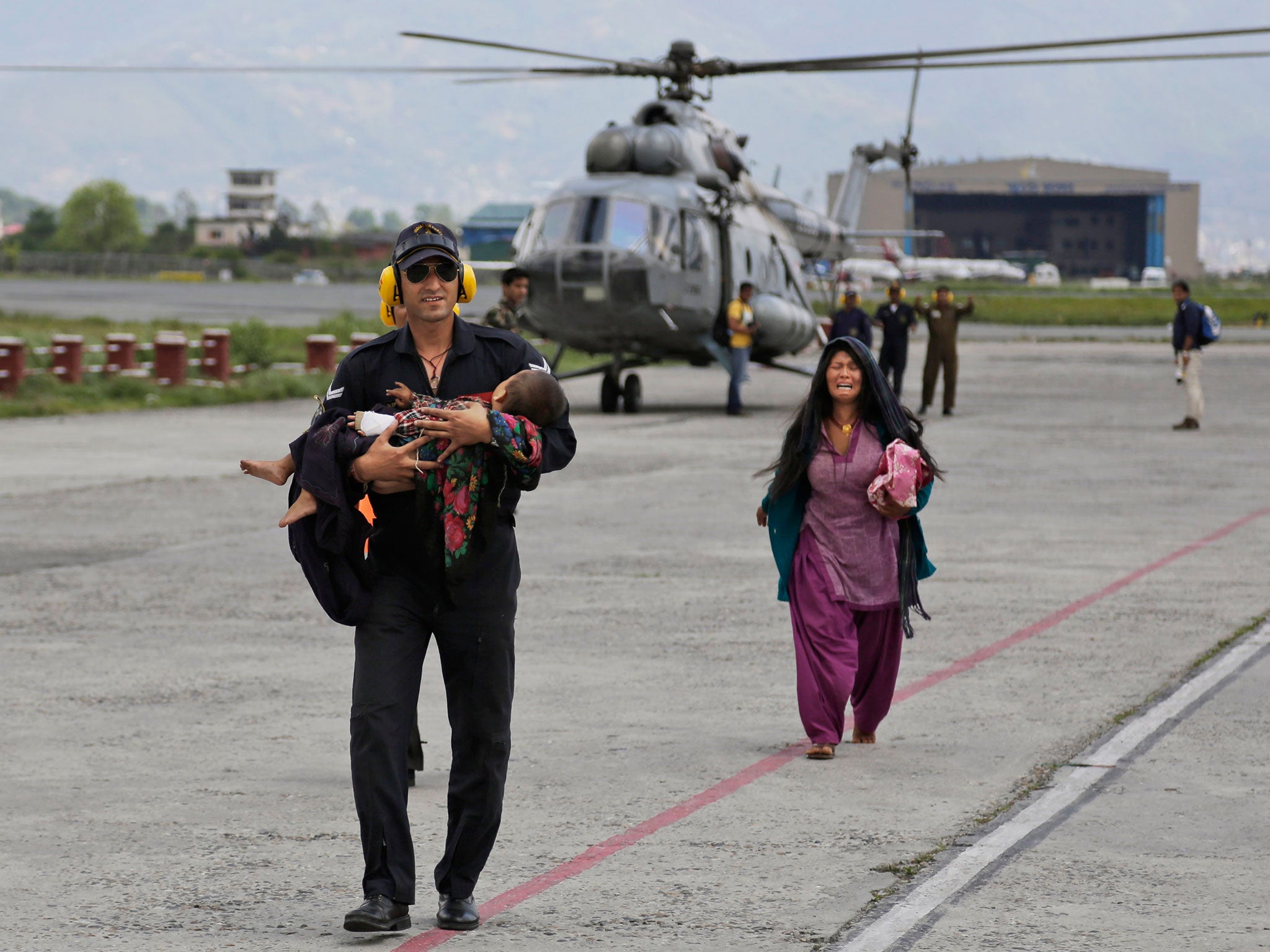 An Indian Air Force person walks carrying a Nepalese child, wounded in the earthquake, to a waiting ambulance as the mother follows