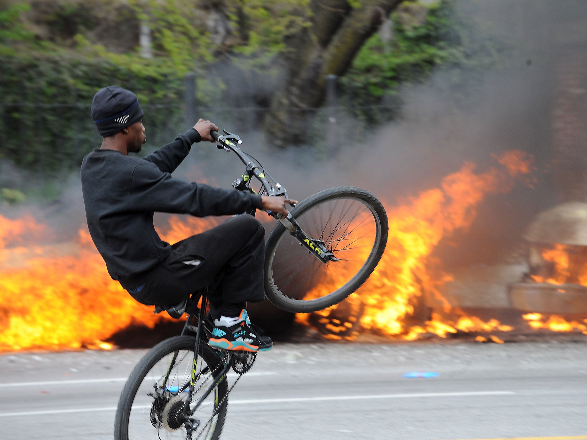 A cyclist rides by burning police cars