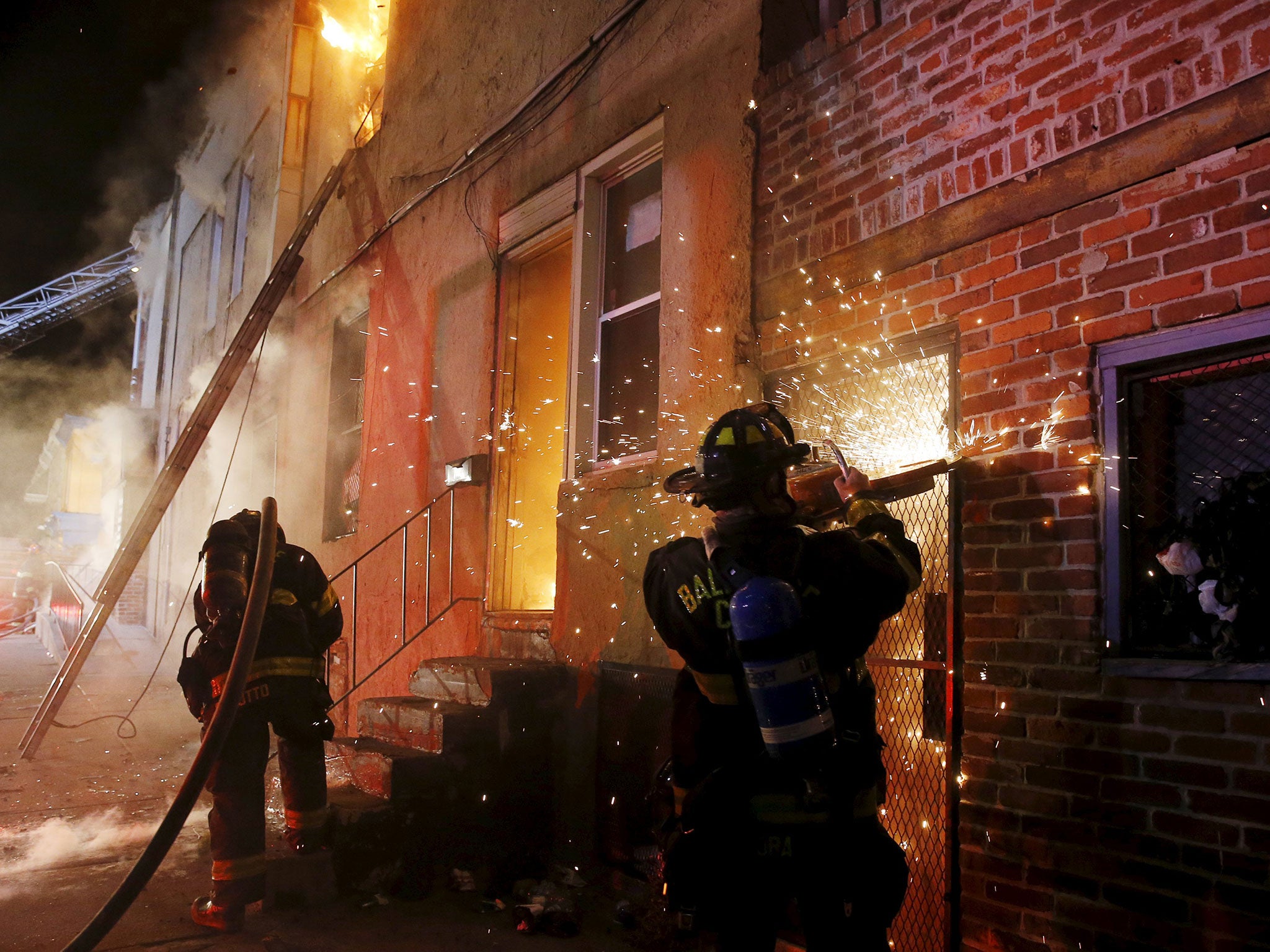 A Baltimore firefighter cuts his way into a burning convenience store with a saw to attack a fire set by rioters at East Biddle Street and Montford Avenue in Baltimore