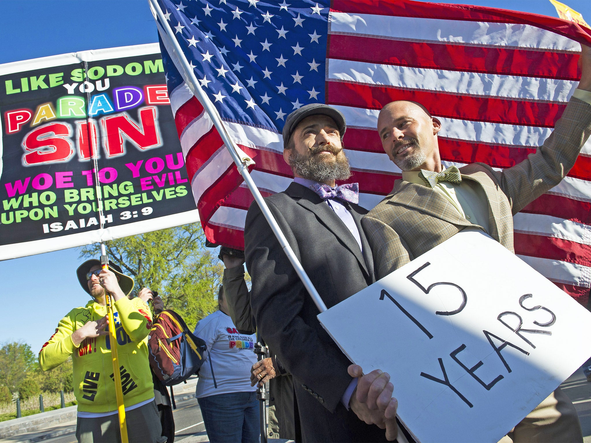 A gay couple hold an American flag in front of the Supreme Court in Washington, while a demonstrator holds a sign denouncing same-sex marriage