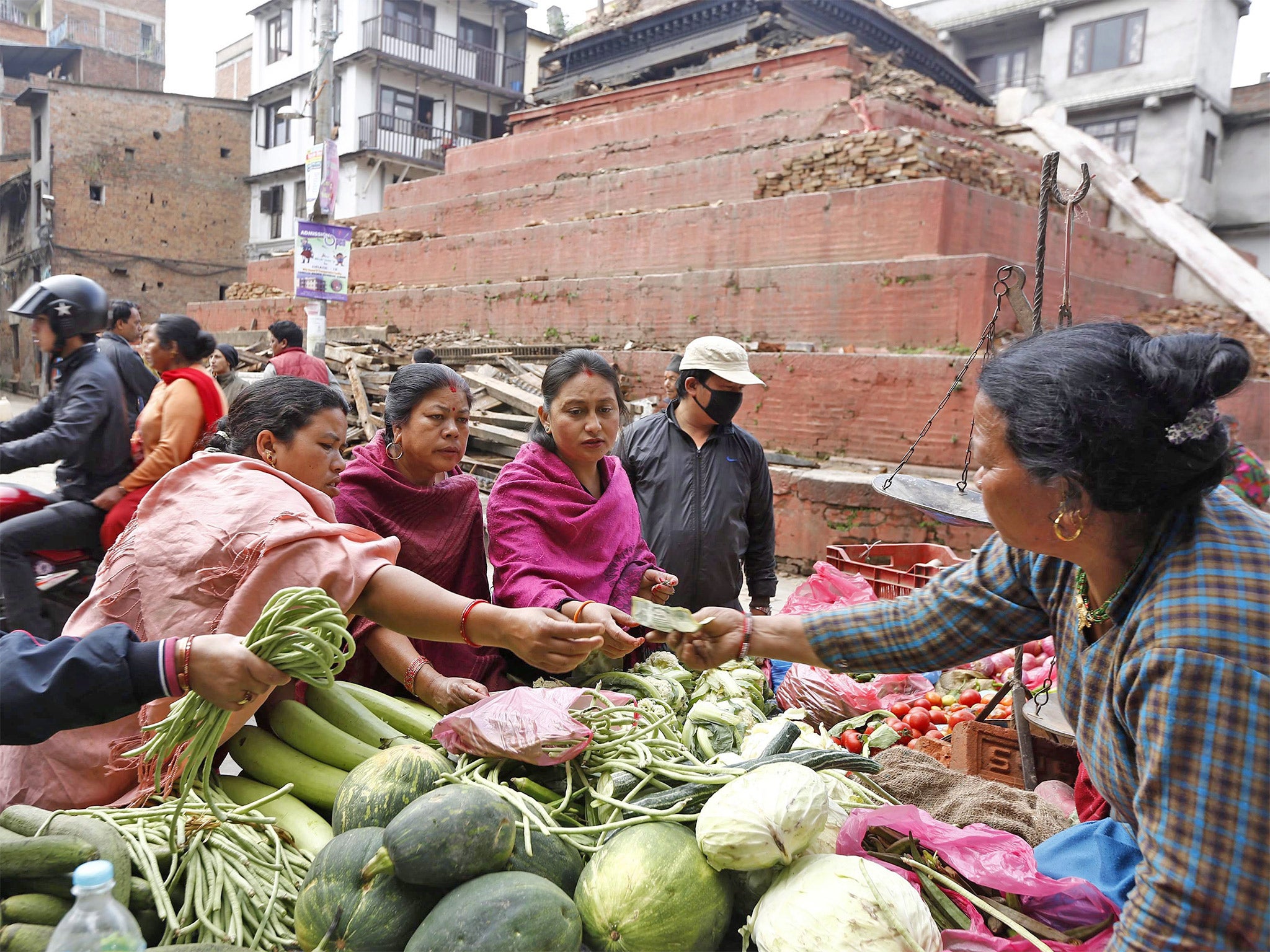 Locals buy vegetables at a street market in front of a damaged temple in Kathmandu