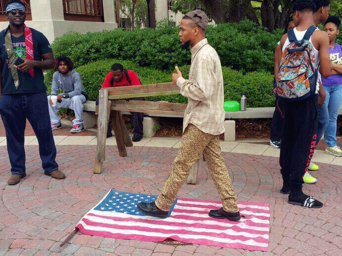 Eric Sheppard, now wanted by police for bringing a gun to a school zone, walking on the American flag at a protest that sparked a number of social media challenges and counter-challenges.