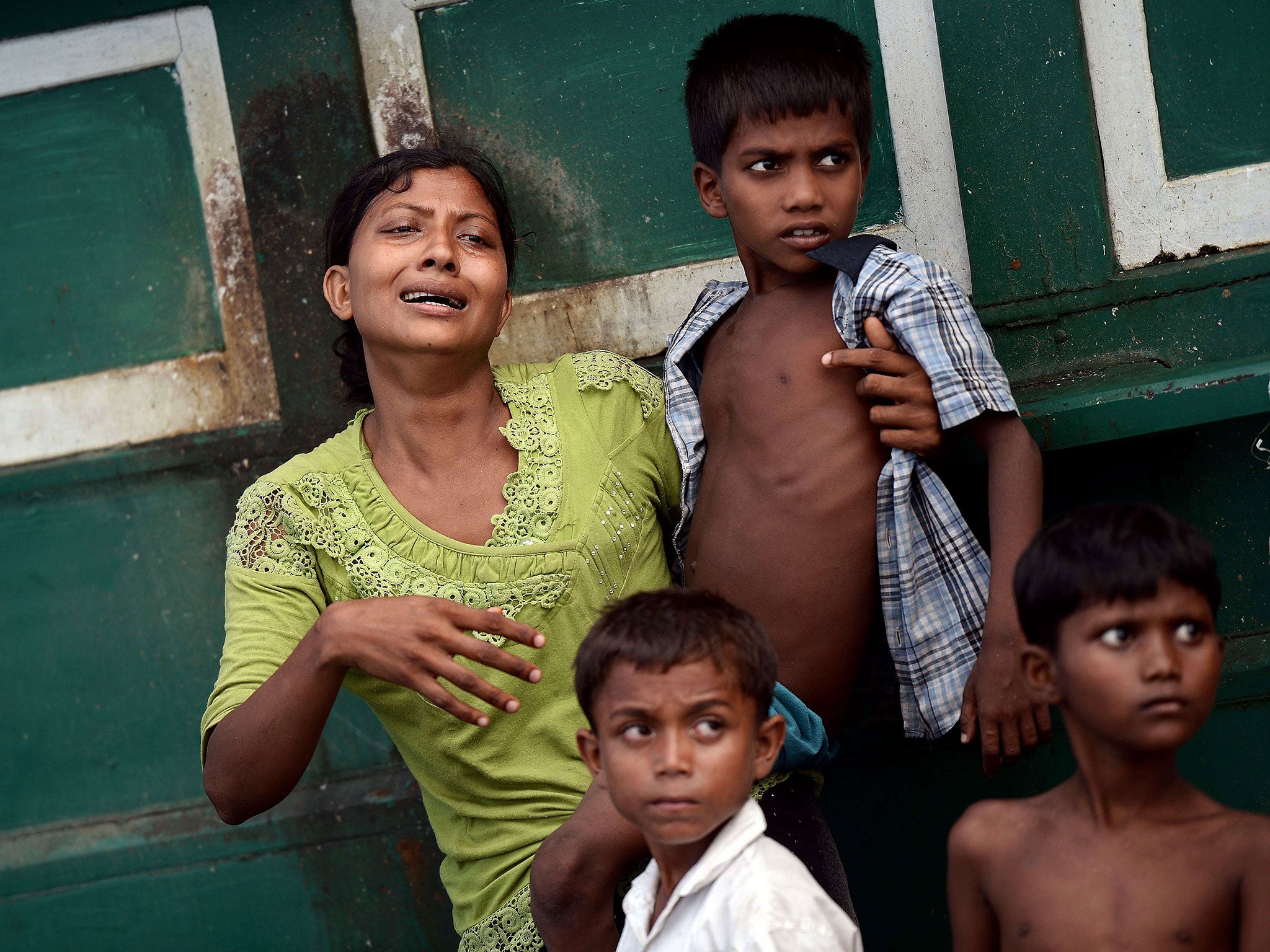 A Rohingya migrant woman holding a child cries as she stands on a boat drifting in Thai waters