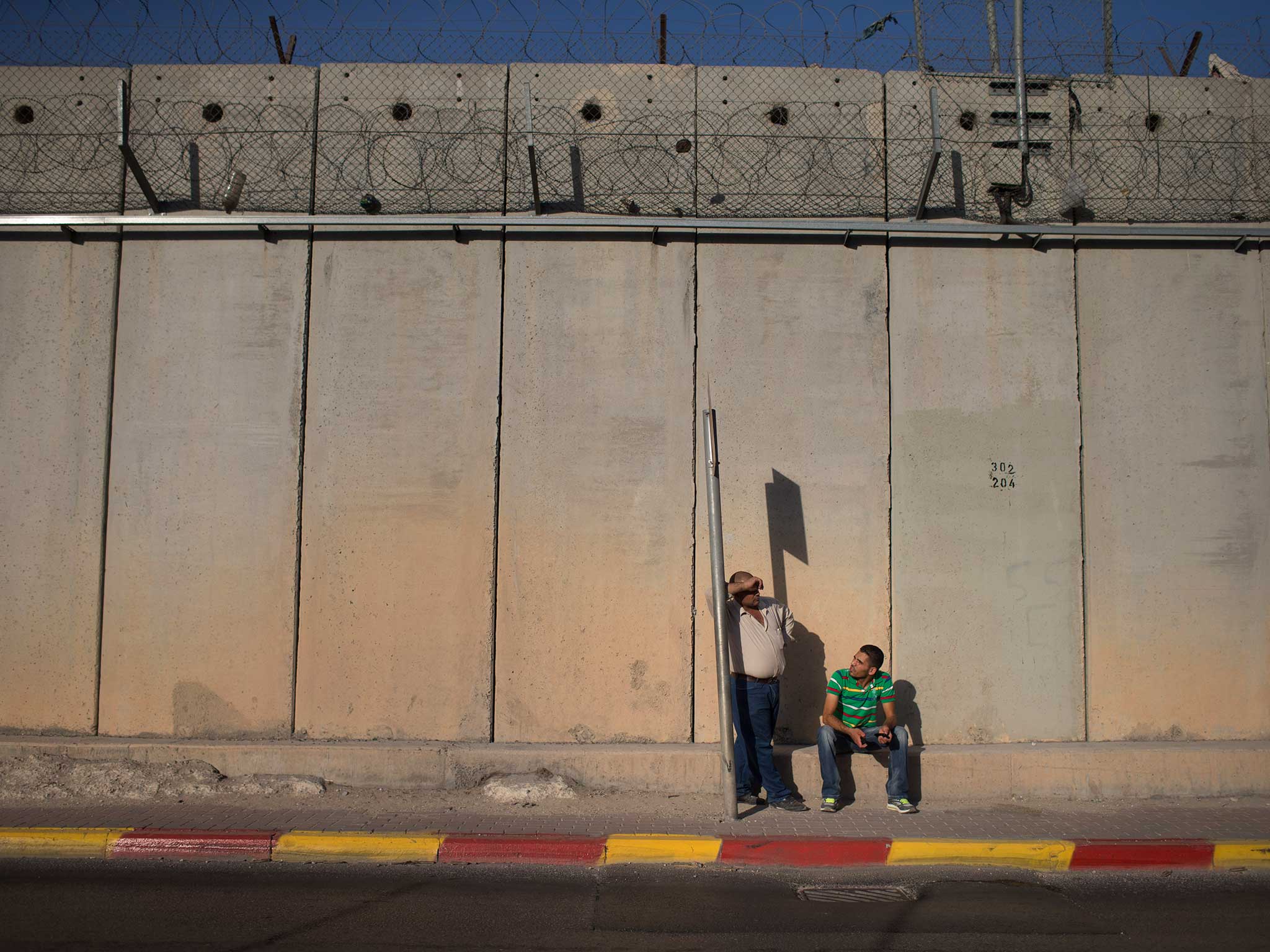 Two Palestinian men wait for a bus along the Isreali West Bank barrier in 2013