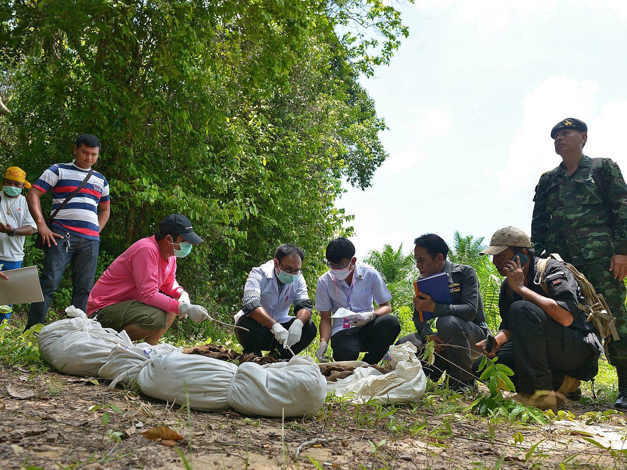 Doctors inspect human remains dug out by rescue workers from graves about one kilometre from the hillside site where shallow graves containing 26 bodies were found