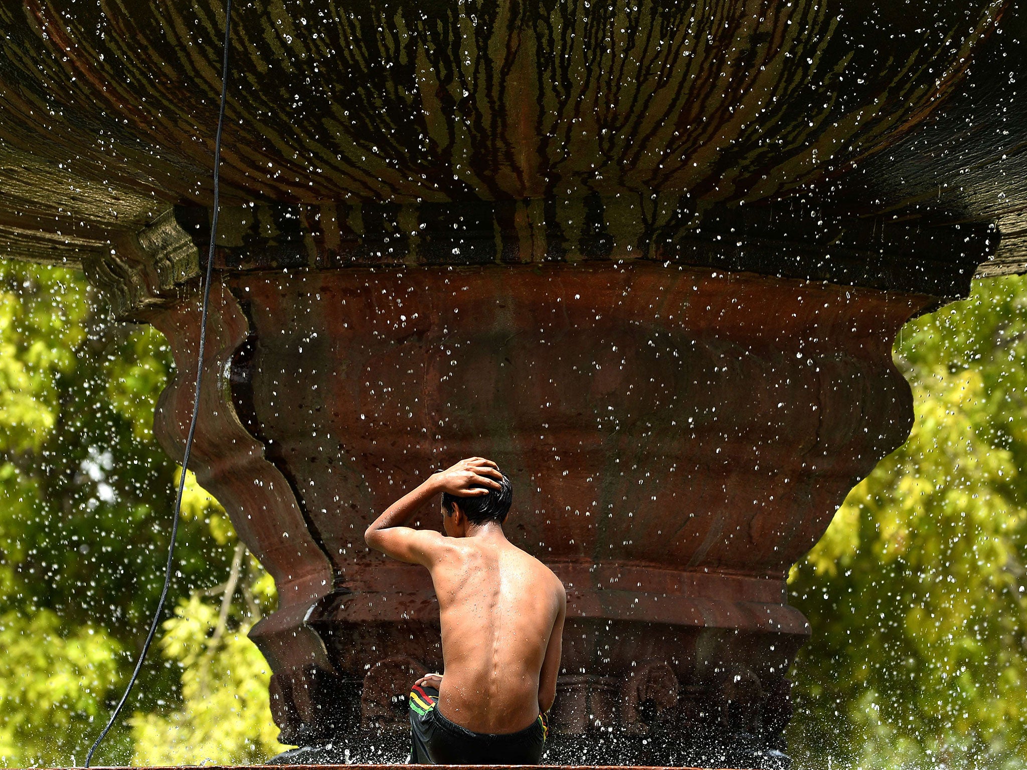 An Indian boy takes a bath at a fountain at India Gate in New Delhi