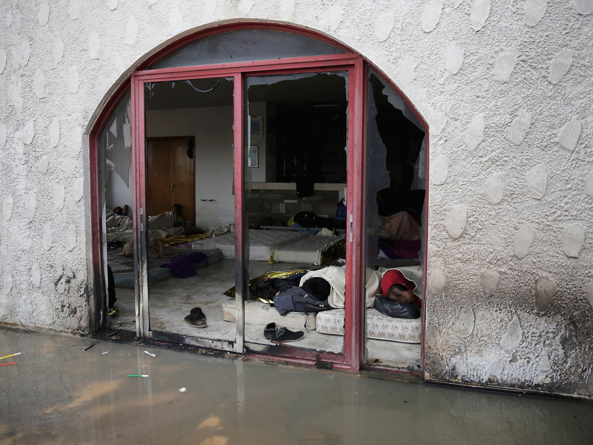 Migrants sleep on the ground next to puddle of water inside an abandoned hotel