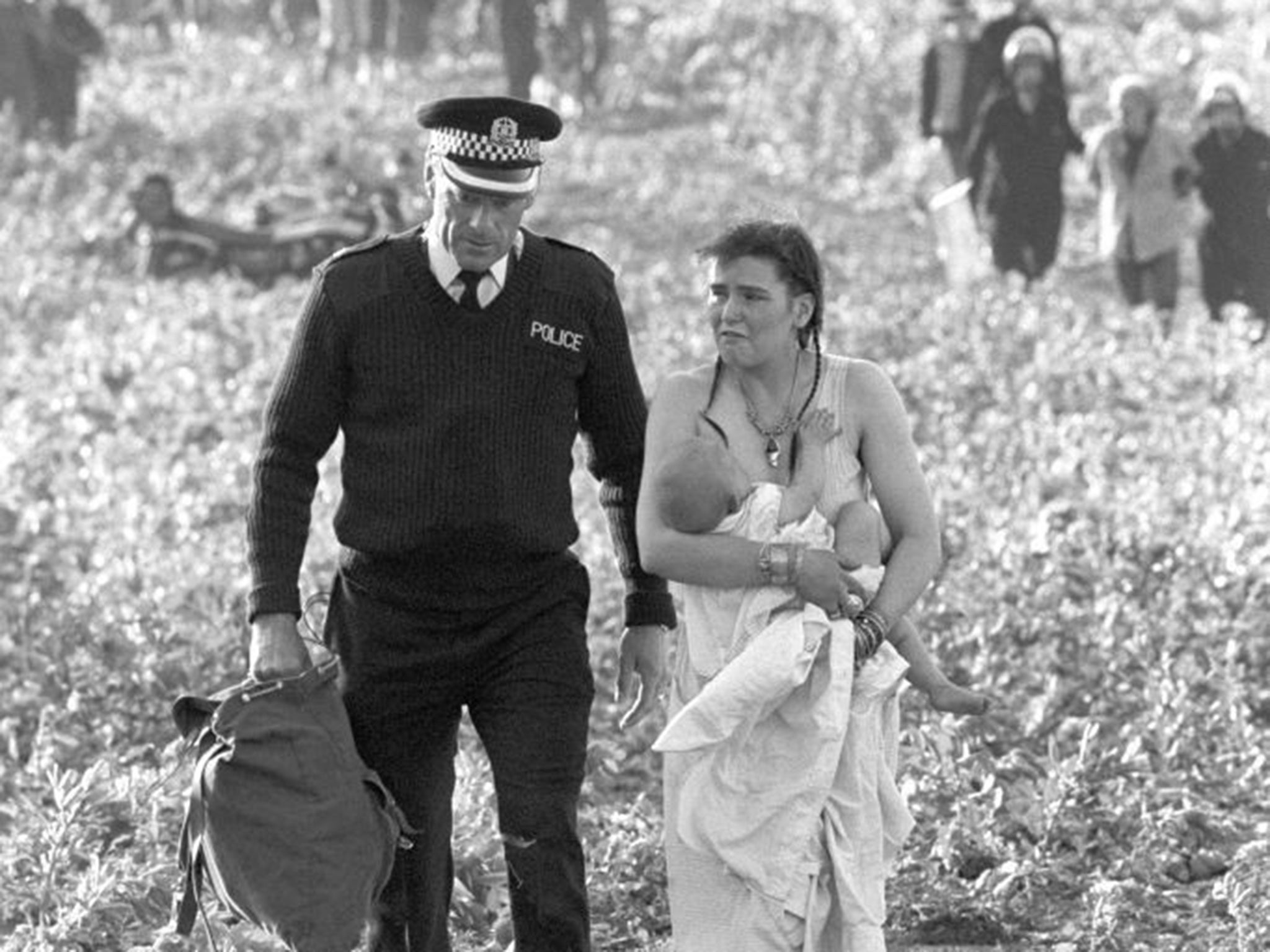 A policeman leads away a woman holding a baby in the field where violence erupted and over 300 people were arrested as police halted a "peace convoy".