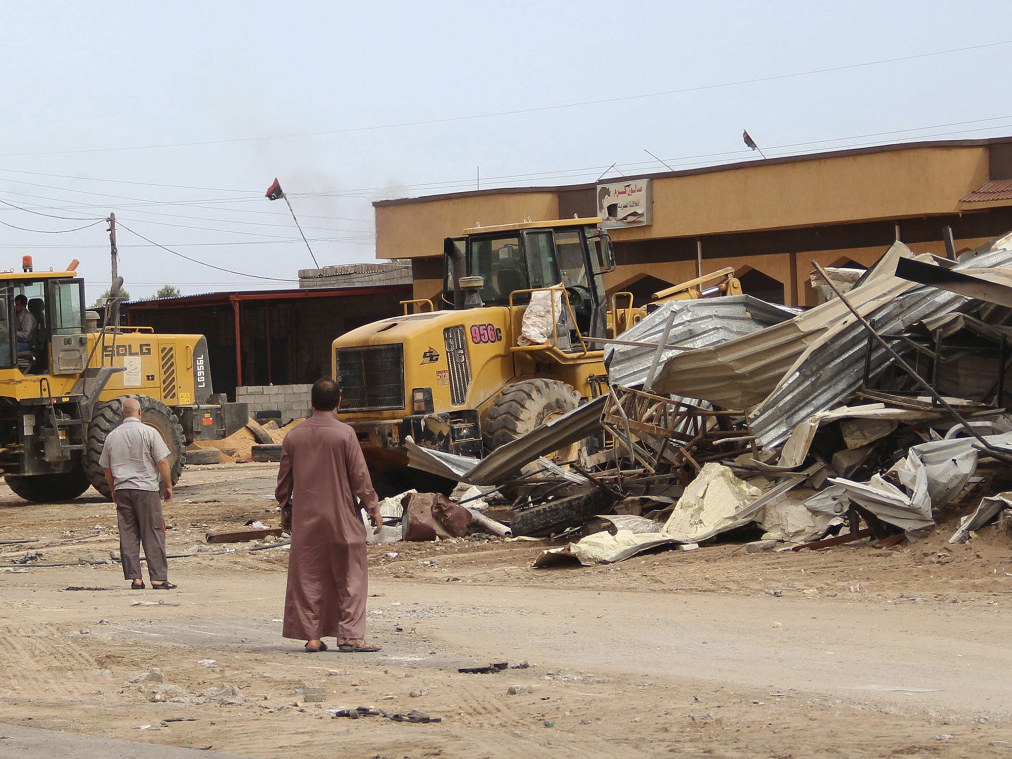 Men watch as bulldozers remove debris in front of a damaged building after a suicide car bomber blew himself up at a checkpoint in Dafniya outside Mistrata, Libya