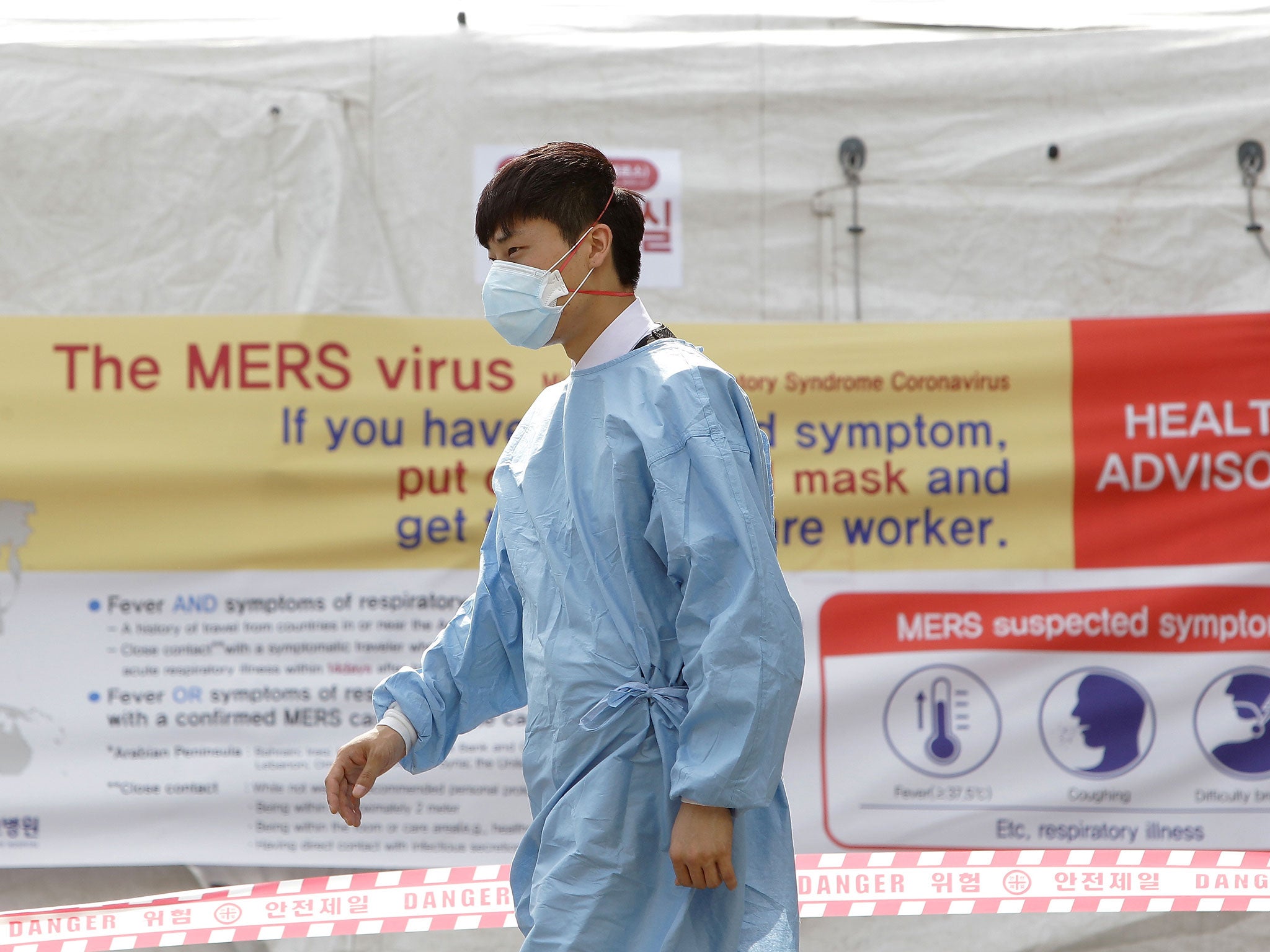 A hospital worker wearing mask walks in front of a health advisory sign at a quarantine tent for people who could be infected with the Mers virus at Seoul National University Hospital